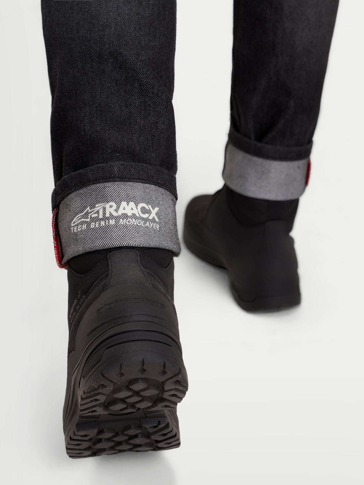 Alpinestars Stella Flex-AST 7 Denim Pants Short, women's motorcycle riding jeans in faded black, rear detail view showing the cuffed selvedge-style edge with A-TRAACX branding and black riding boots worn by a model