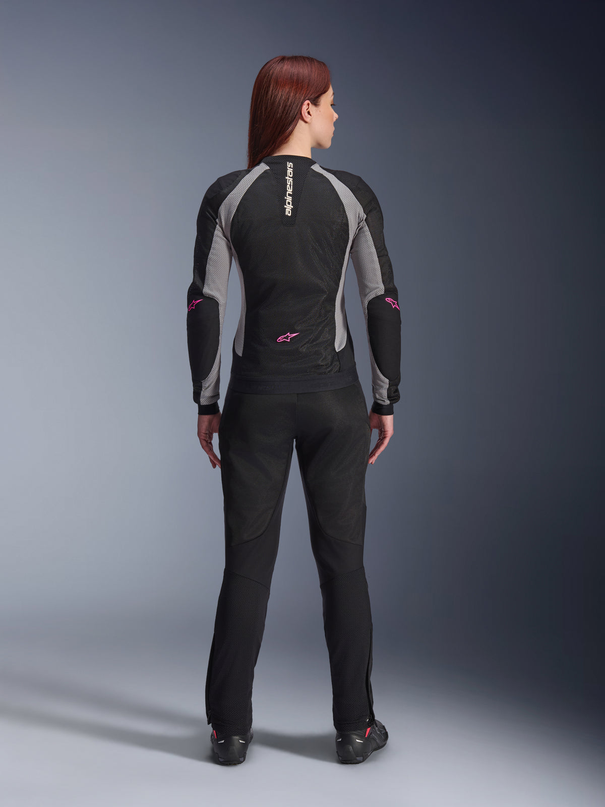 Alpinestars Stella Troop-Air byxor för dam i svart, vy bakifrån, kombinerade med en svart och grå mc-jacka i mesh med rosa detaljer, studiobild som visar den tekniska ventilerade textildesignen.