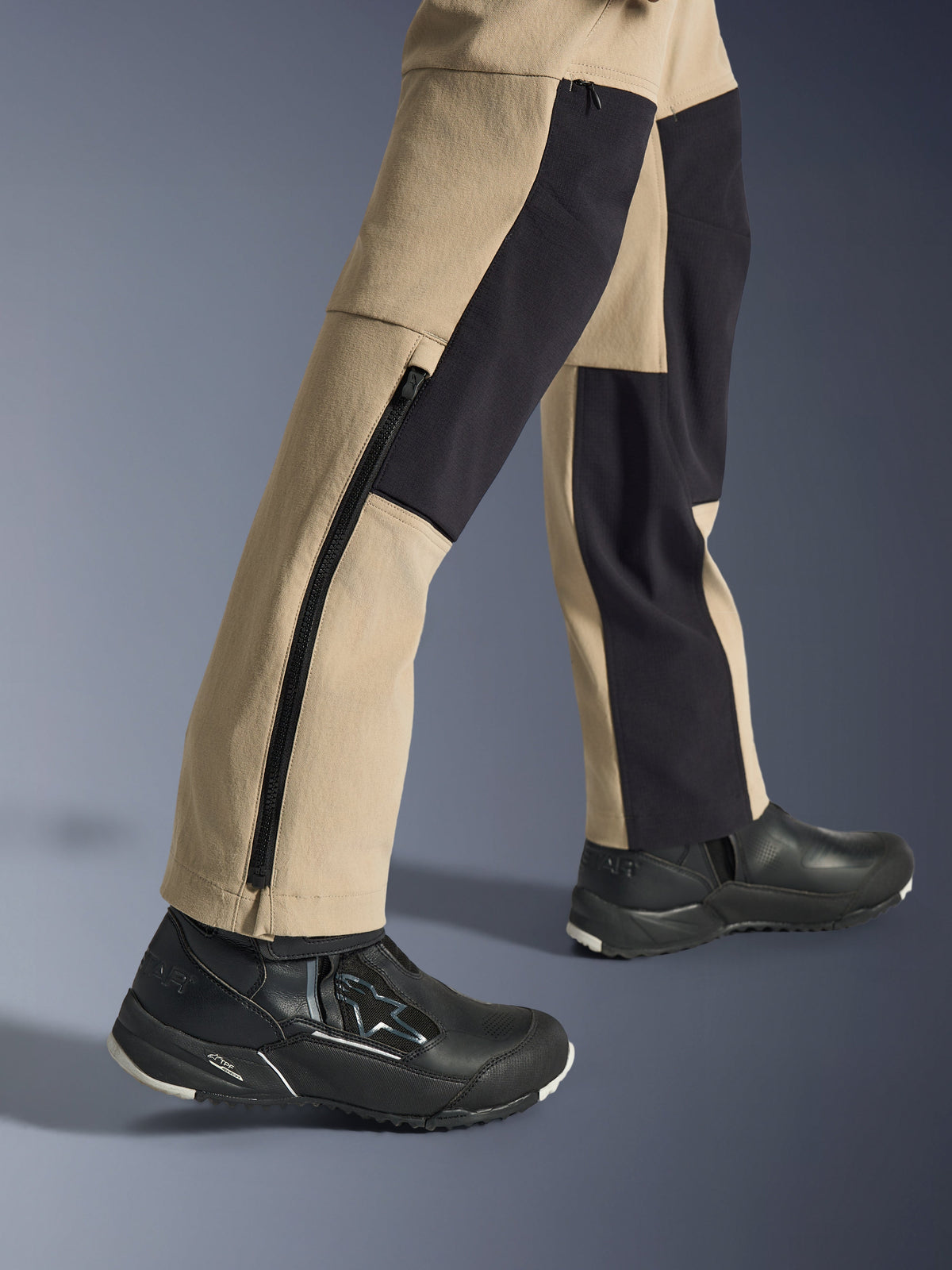 Alpinestars Stella Flex-AST Explorer-byxor för dam, adventurebyxor för motorcykel, sandfärgade och svarta, närbild av underbenen och anklarna med en lång sidodragkedja och svarta förstärkningspaneler, bärs med svarta Alpinestars körskor.