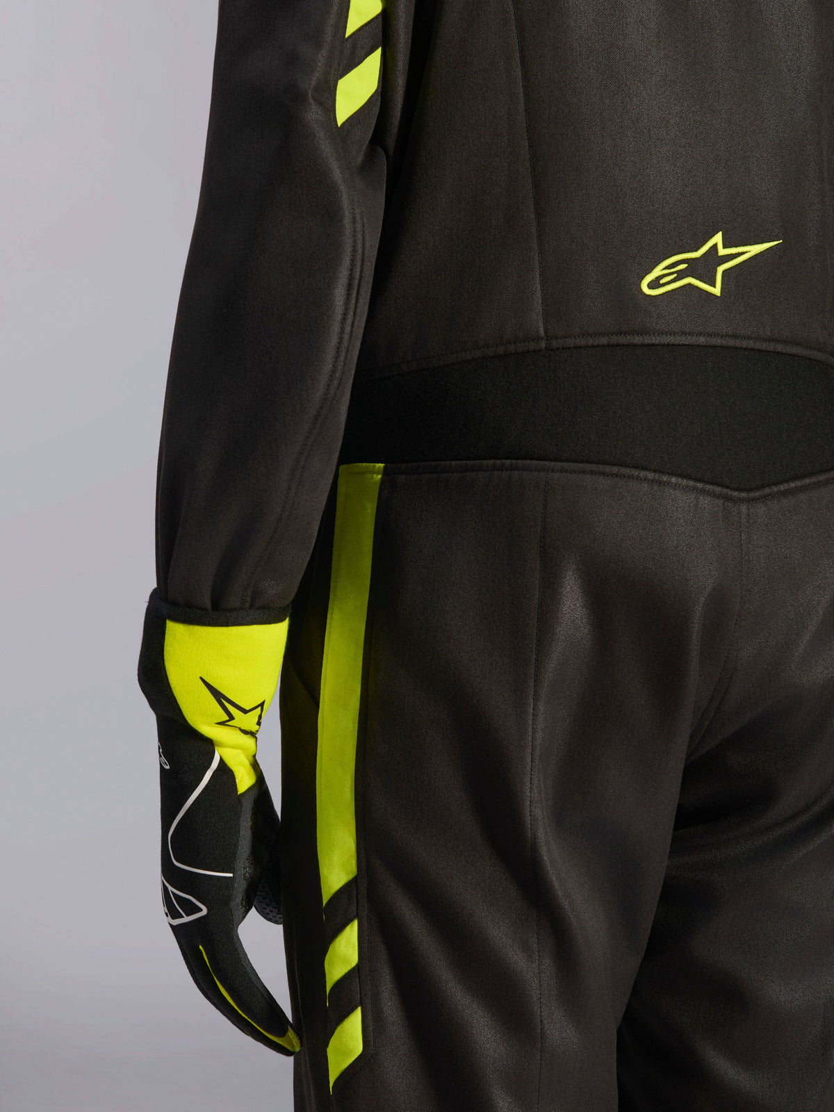 Alpinestars GP Race V3 Suit FIA, svart och fluorescerande gul, närbild på detaljer vid midjan och benets sida, med stretchpaneler i aramid och en matchande racinghandske, professionell bilracingutrustning