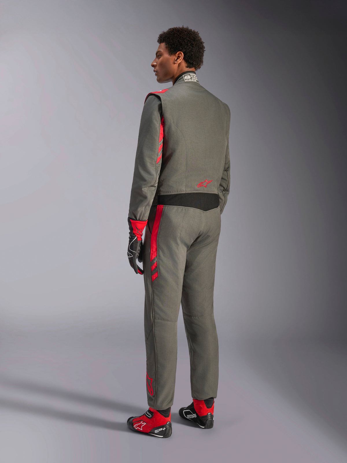 Alpinestars GP Race V3 Suit FIA, antracitgrå och röd racingoverall, bakifrån vy av modell i tvålagersdräkt, röda detaljer på axlar och ben, matchande handskar och skor, professionell racingutrustning