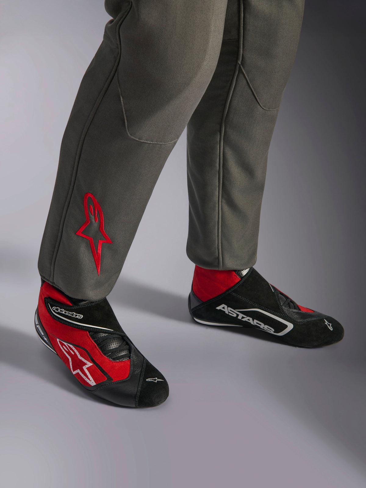 Alpinestars GP Race V3 Suit FIA, Anthracite Red racingoverall, närbild på underbenen med broderad röd stjärnlogotyp, kombinerad med röda och svarta racingskor, professionell motorsportutrustning designad för förarskydd och komfort