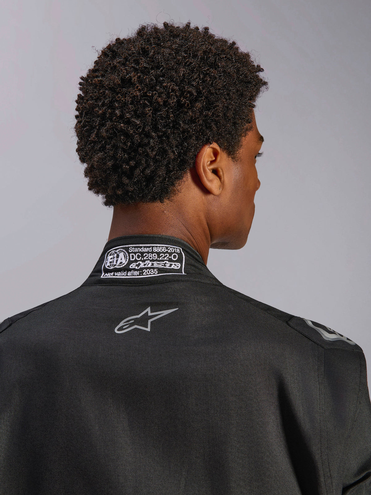 Alpinestars Hypertech V3 Suit, Black Dark Shadow, närbild bakifrån av kragen med FIA 8856-2018-certifieringsetikett och logotyp på ryggen, professionell lättvikts racingoverall med atletisk passform
