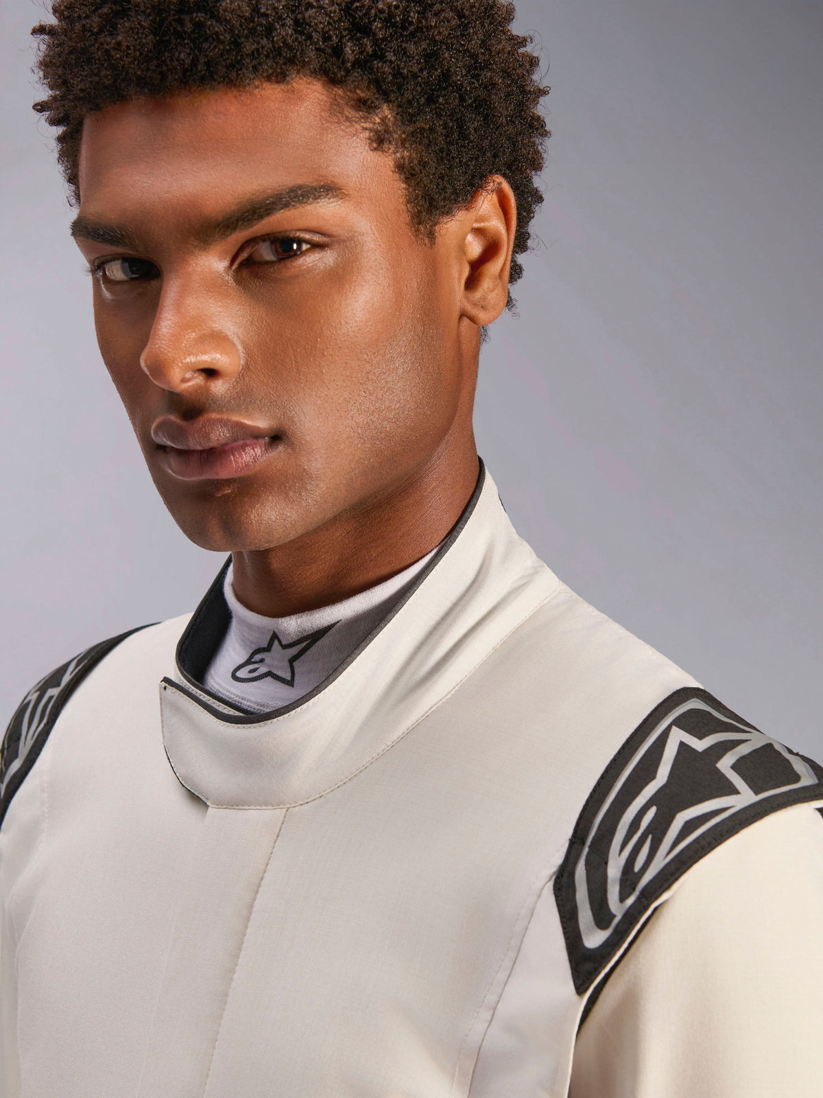 Närbild på en manlig modell som bär Alpinestars Hypertech V3 Suit i White Black Silver, med en hög krage med säker stängning och Alpinestars-logotyper på axlarna, professionell racingutrustning.
