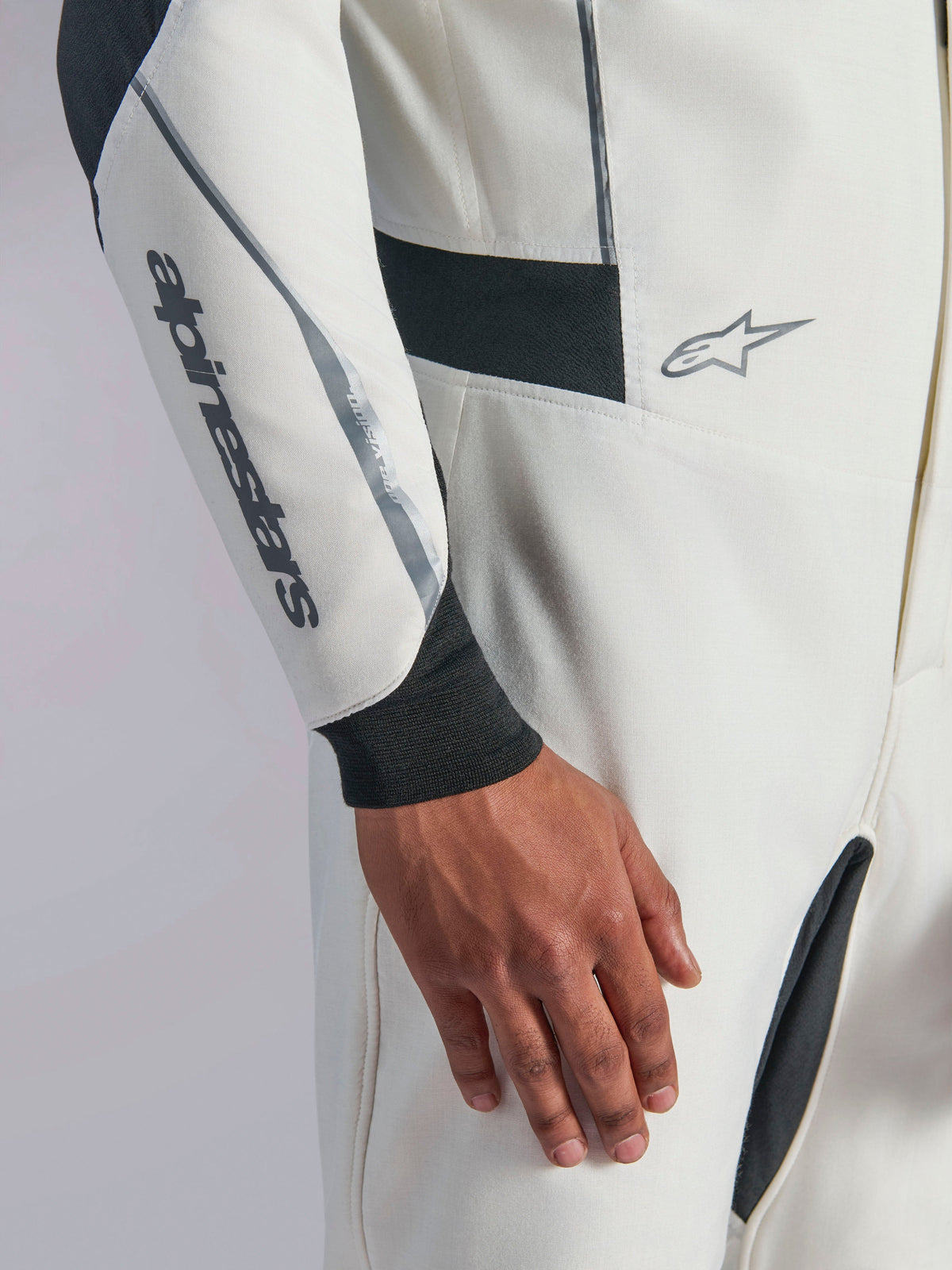 Alpinestars Hypertech V3 Suit, närbild på vit racingoverall med svarta och silverfärgade detaljer, Alpinestars-logotyp på underarmen, svart stickad mudd vid handleden och mörka stretchpaneler för rörlighet, professionella motorsportkläder.