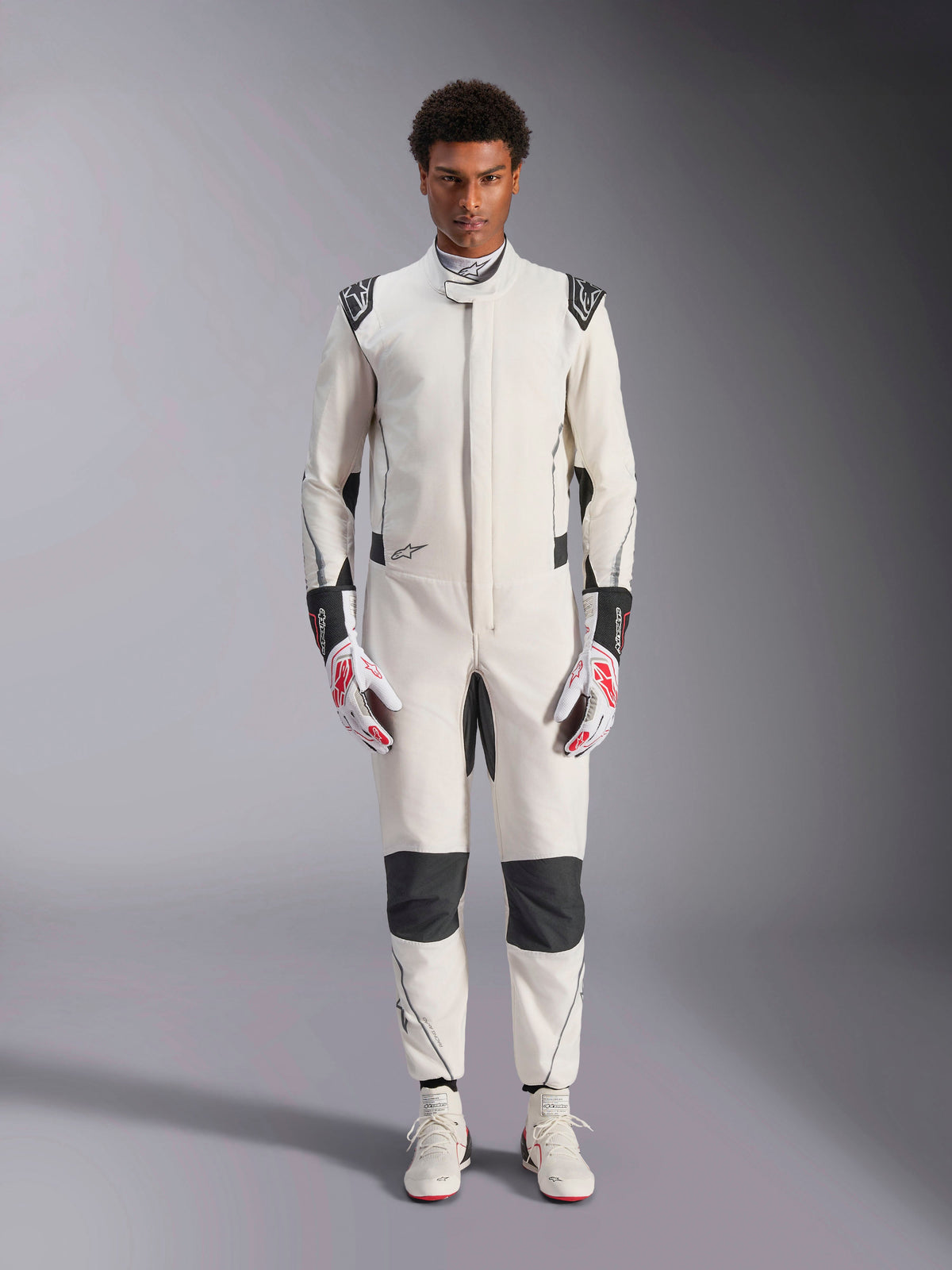 Alpinestars Hypertech V3-dräkt, professionell racingdräkt för bilsport, vit, svart och silver, bärs av en modell med röd-vita handskar och matchande vita racingskor, med svarta kontrastpaneler och Alpinestars-logotyper, atletisk slim fit-design