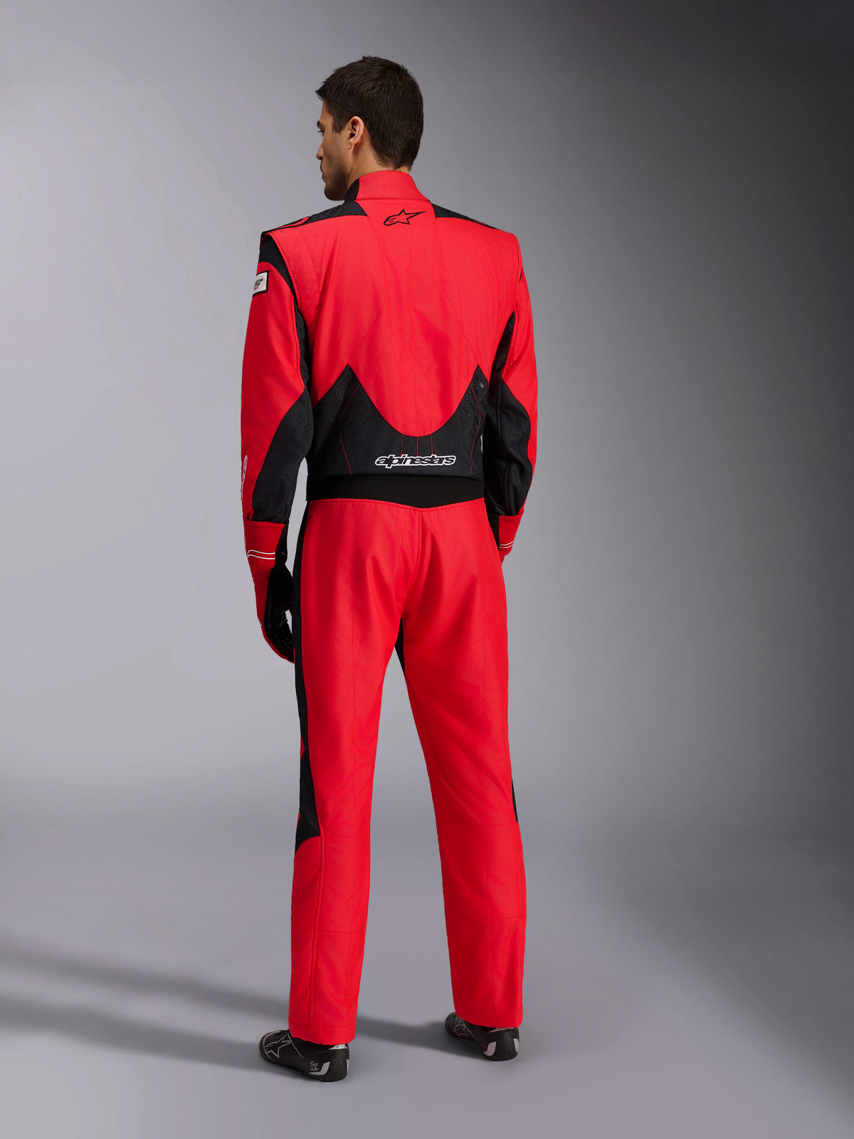 Helfigur bakifrån av Alpinestars GP Pro Comp V2 FIA racingoverall, röd och svart, med svarta meshpaneler som andas på axlarna och i ländryggen, vit Alpinestars-logotyp, bärs med matchande racinghandskar och stövlar, professionell förarutrustning för motorsport