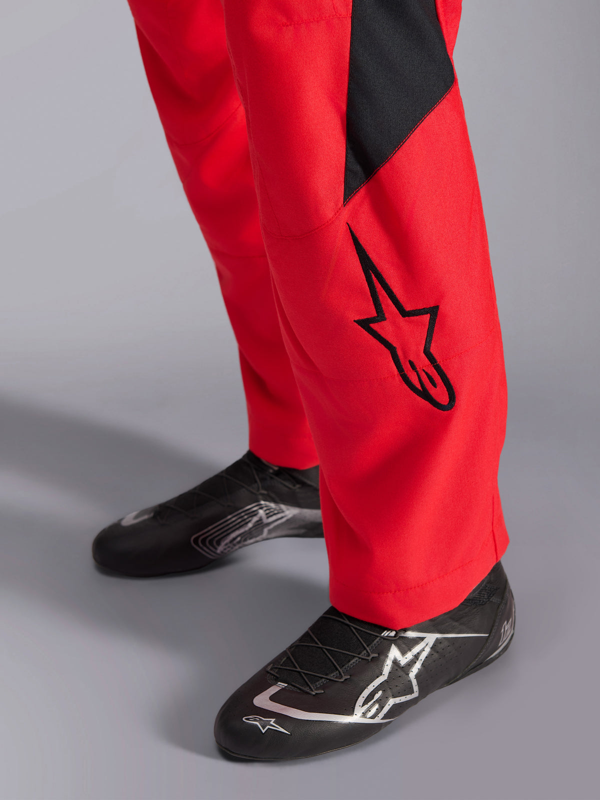 Alpinestars GP Pro Comp V2 FIA racingoverall, närbild på underbenet och racingskor, röd med svart Astars-logotyp och panel, matchad med svarta högpresterande racingskor, bilracingutrustning.