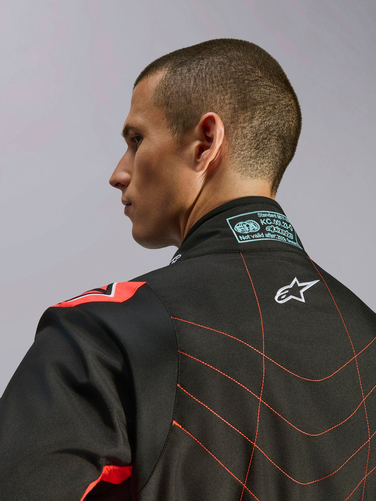 Alpinestars KMX-9 V3 Suit, Black and Red Fluo Karting Suit, close-up view of the upper back and collar on a model, featuring white Alpinestars logo, intricate red stitching, and FIA certification label on the neck