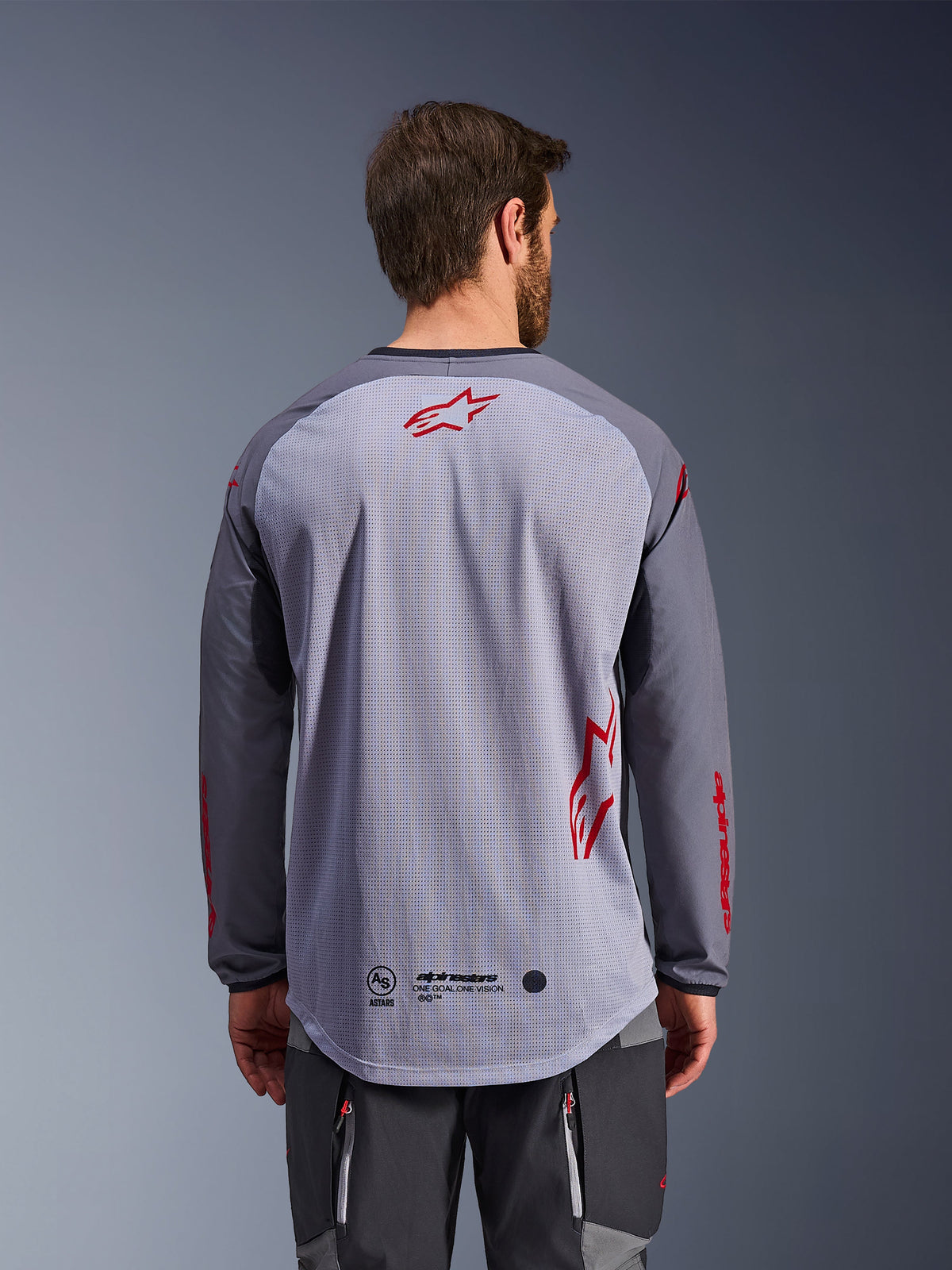 Alpinestars Maxdura Dual Jersey, Rear View, Mid Gray and Dark Gray, featuring a breathable mesh back with red Alpinestars star logos, long sleeves, and an extended drop-tail hem, adventure motorcycle gear