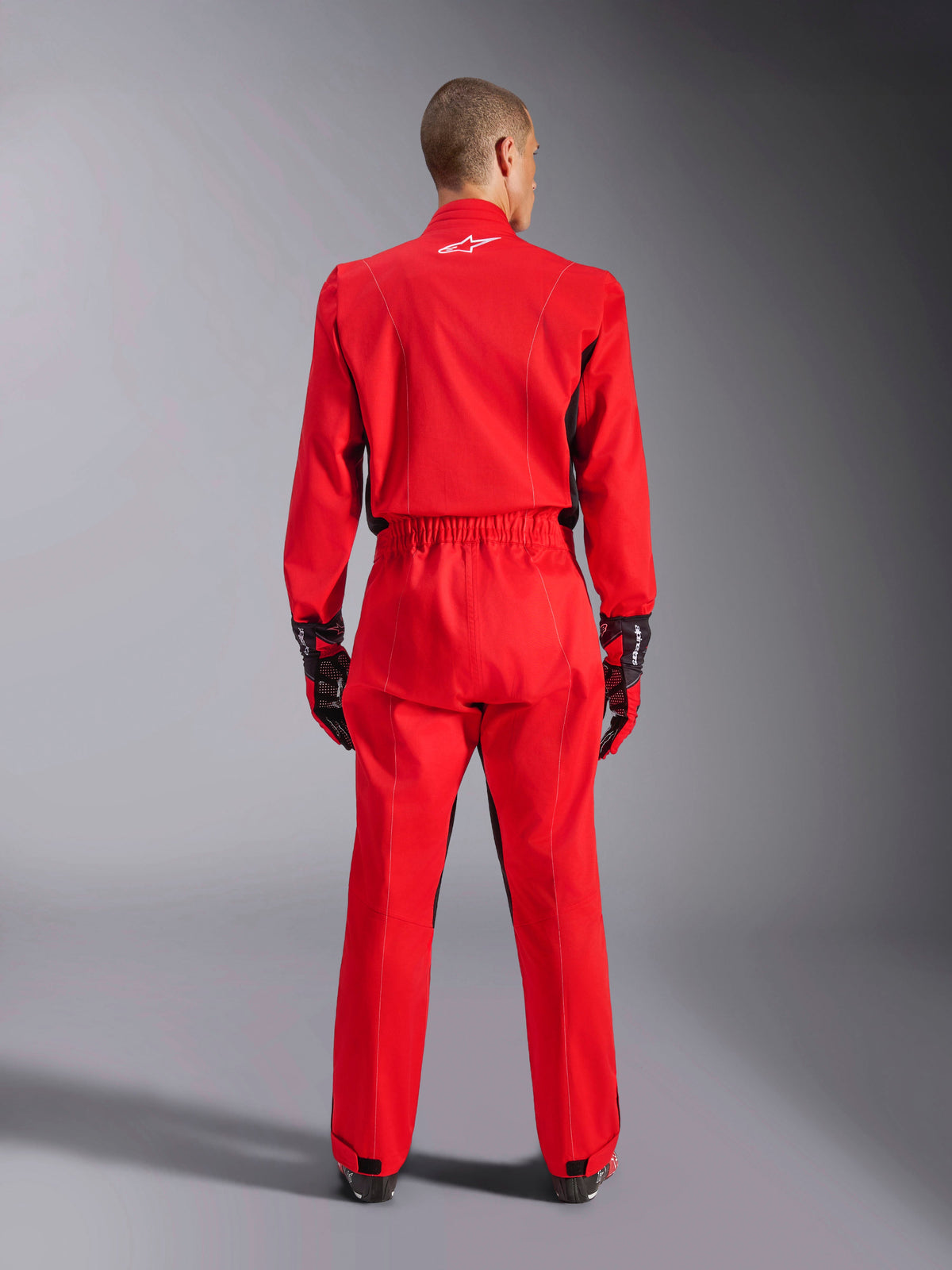 Alpinestars Kart Indoor V2 Suit, Red Karting Suit, back view showing elastic waistband and white star logo on the neck, worn with black and red racing gloves, designed for indoor and recreational karting