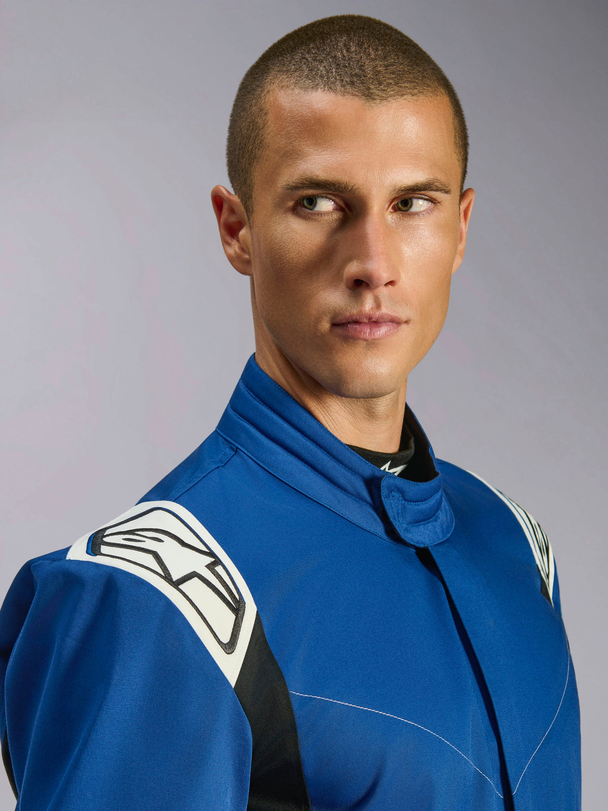 Alpinestars Kart Indoor V2-overall, blå kartingdräkt, närbild av manlig modell, vita axelpaneler med svart stjärnlogotyp, ergonomisk krage, slitstarkt enkellagers twill för rekreationsracing