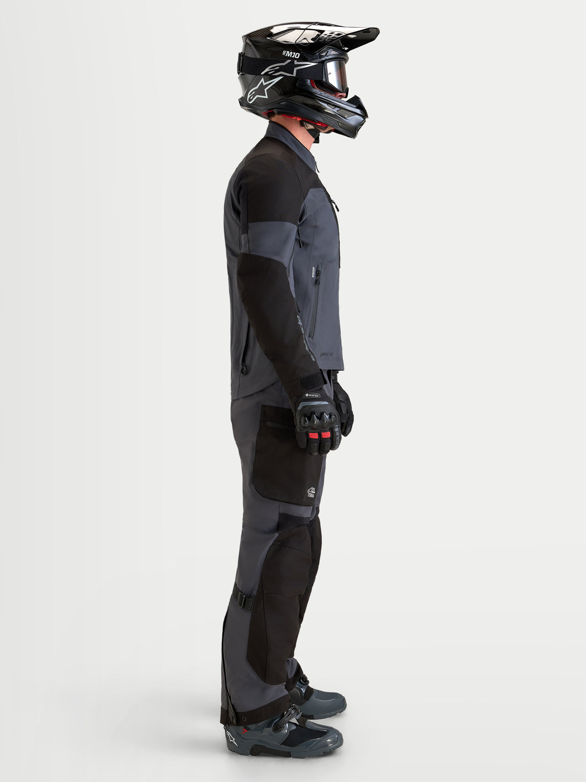 Alpinestars Arenis Gore-Tex gear set, äventyrsmotorcykeljacka och byxor för herr, svarta och mörkgrå, sidoprofilvy på modell som bär matchande hjälm och stövlar, vattentät all-terrain-körutrustning