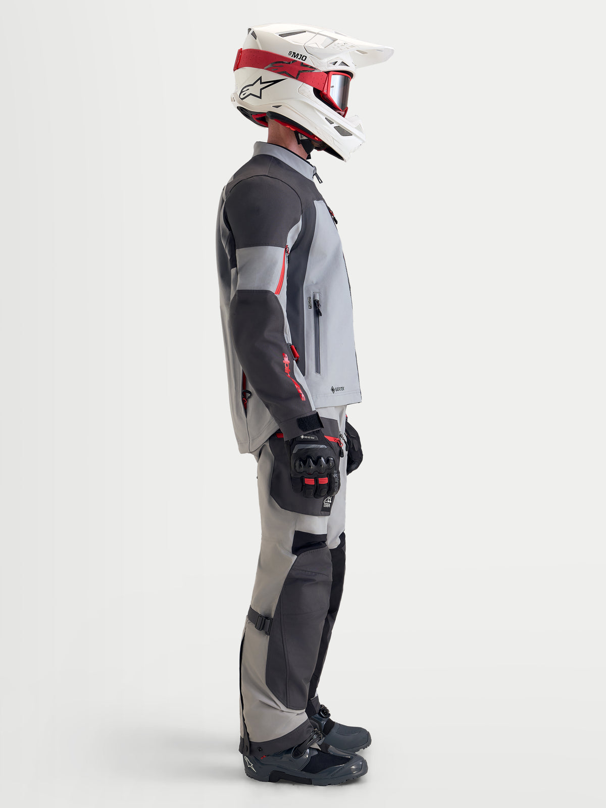 Alpinestars Arenis Gore-Tex jacka, äventyrsmotorcykeljacka för herr i mellanmörk grå, mörkgrå och svart, sidovy av en förare som bär den vattentäta textiljackan med matchande utrustning samt vit och röd hjälm