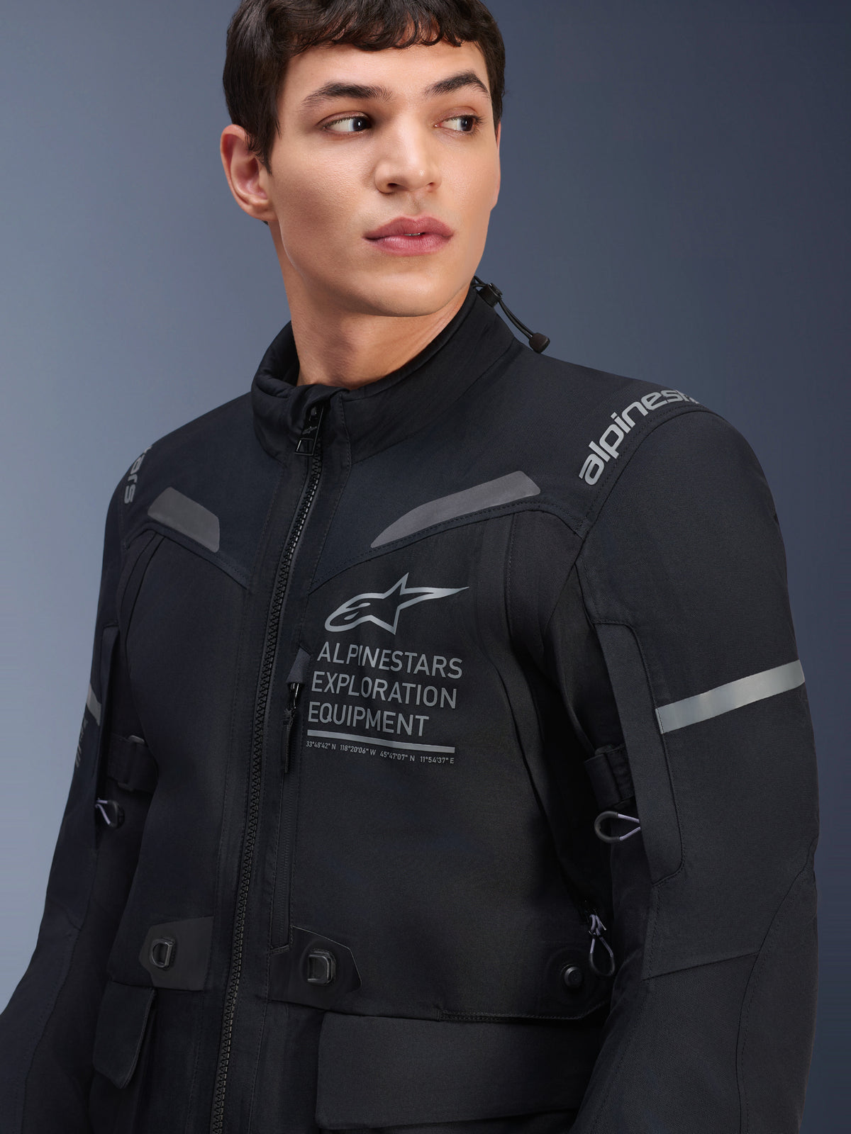 Alpinestars ST-7 2L GORE-TEX-jacka, motorcykeljacka, svart och mörkgrå, bärs av en manlig modell, med Alpinestars Exploration Equipment-logotyp på bröstet, grå reflexdetaljer och textilkonstruktion redo för äventyr