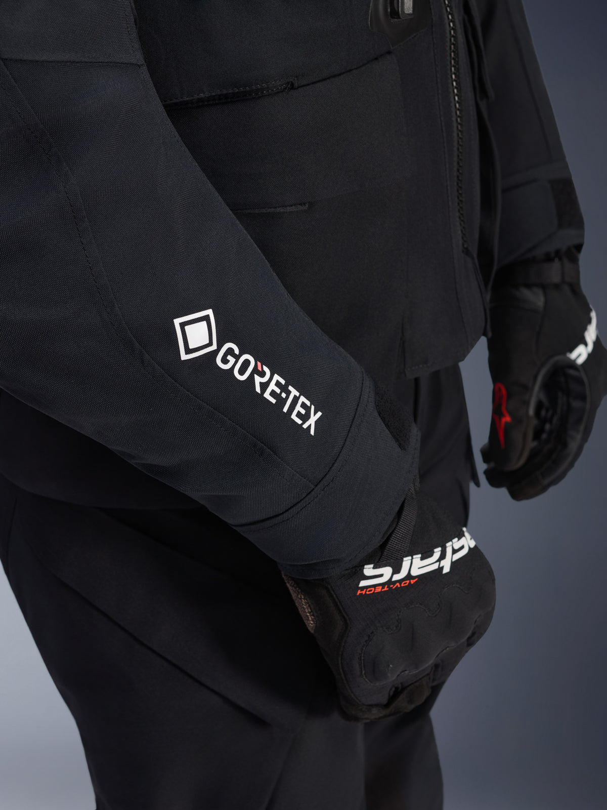 Alpinestars ST-7 2L GORE-TEX-jacka, svart och mörkgrå, närbild på ärm med vit GORE-TEX-logotyp, bärs med svarta adventure-körhandskar, vattentäta motorcykelkläder