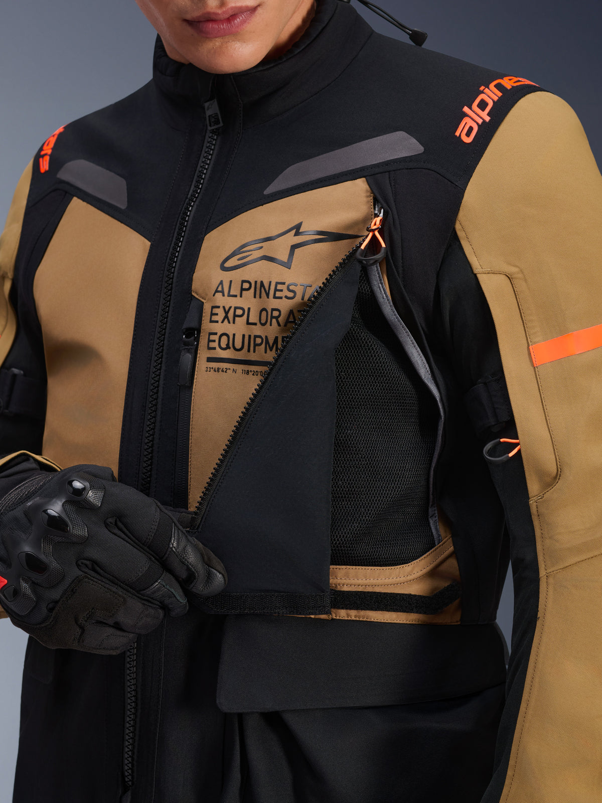 Alpinestars ST-7 2L GORE-TEX-jacka, motorcykeljacka för adventure touring, Gobi Brown och svart, närbild som visar den öppnade ventilationspanelen på bröstet som avslöjar ventilerande mesh, med Alpinestars Exploration Equipment-logotyp och orange detaljer.