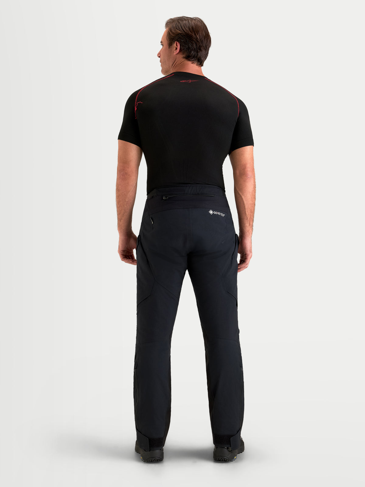 Alpinestars St-7 V2 2L Gore-Tex Pants Short, men's adventure touring motorcycle pants in black, rear view on a model wearing waterproof textile gear and a matching dark top.