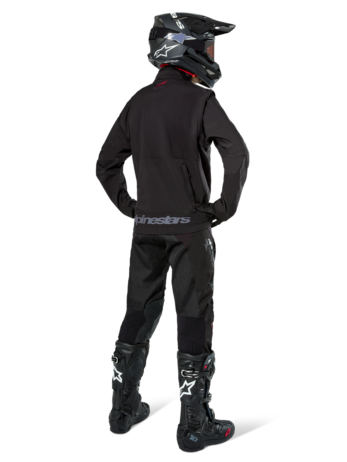 Enduroförare sedd bakifrån i Alpinestars Lite-Dura Softshell Jacket i svart, matchad med svarta tekniska körbyxor och stövlar, med en bakre förvaringsficka med dragkedja och Alpinestars-logotyp i nederkanten, komplett offroad-utrustning för motocross.