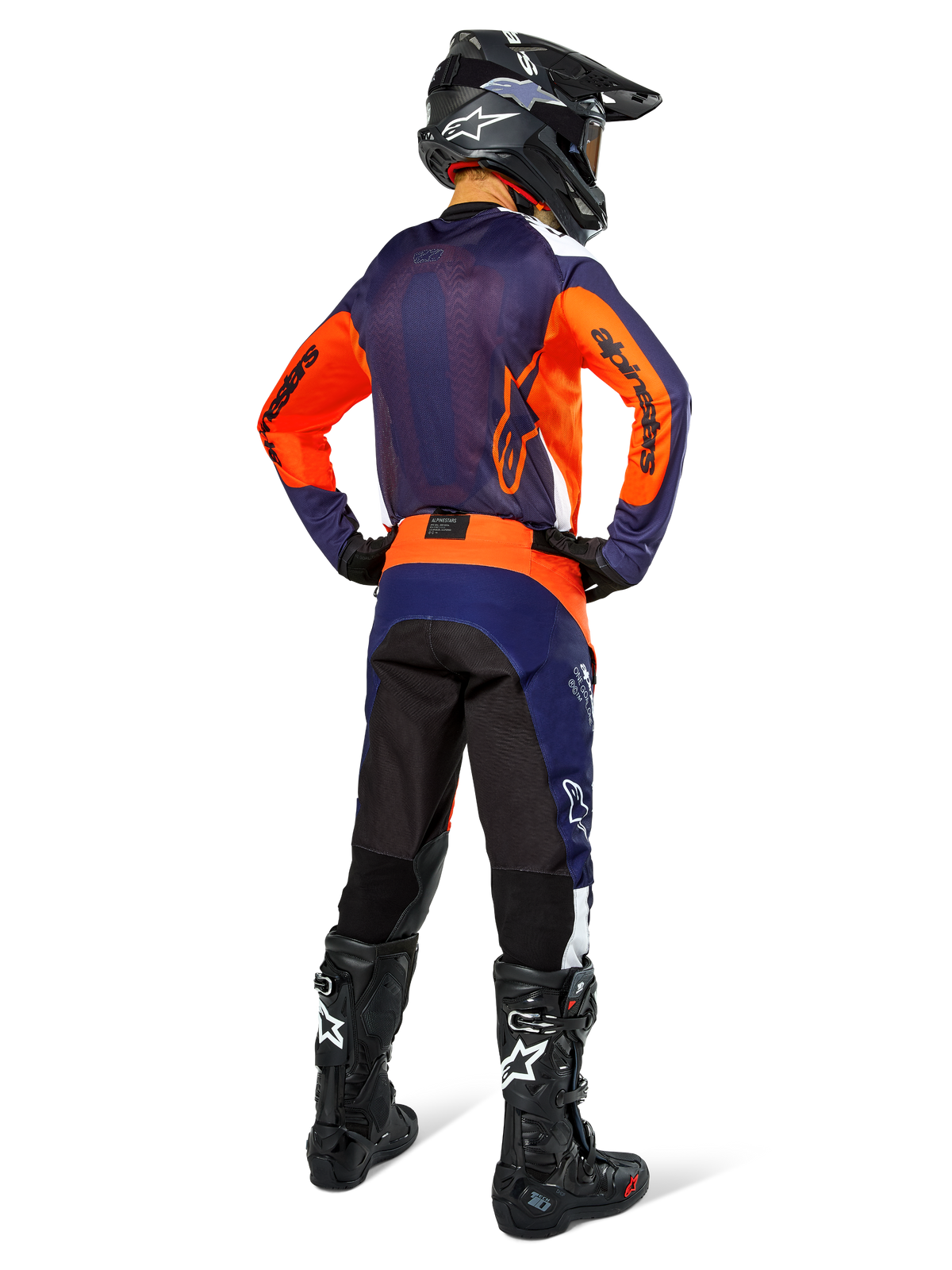 Motocrossförare i komplett racingutrustning sedd bakifrån, marinblå och orange tröja, Pro-Dura-byxor i marinblått, starkt orange och vitt, svart hjälm och svarta stövlar, professionell outfit för offroad-racing.