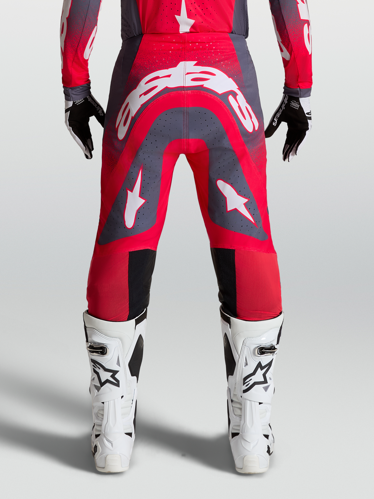 Alpinestars Supertech Hiten AFD byxor, motocrossbyxor för herrar, röd fluor och grå med vita logotyper, vy bakifrån på modell med vita stövlar.
