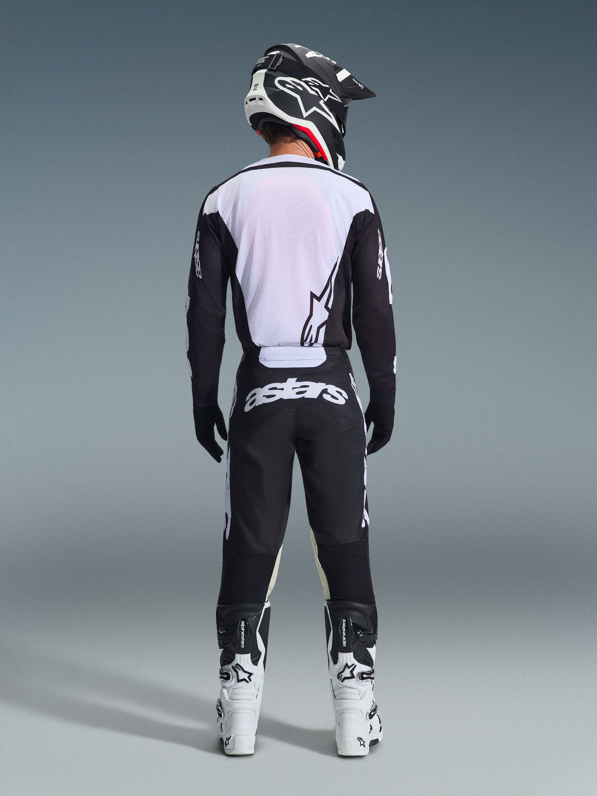 Motocrossförare sedd bakifrån bär Alpinestars 2026 Racer Air Riway-byxor i svart och vitt, matchande svartvit långärmad tröja, vita och svarta racingstövlar och en svart hjälm med Alpinestars-märkning.