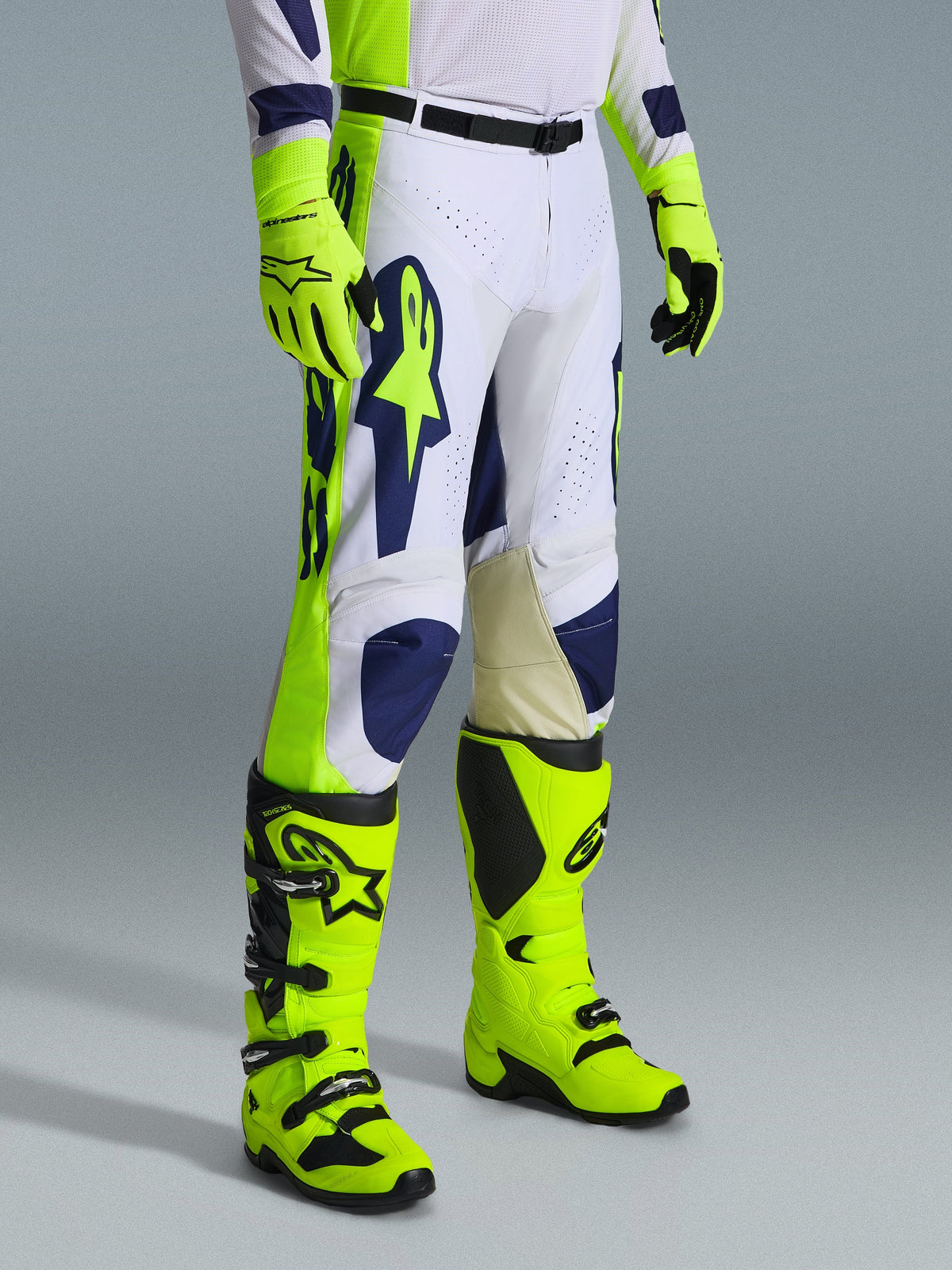 Alpinestars 2026 Racer Air Riway byxor, motocrossbyxor, ljusgrå, neongula och blå, bärs med matchande neongula handskar och stövlar, med stor blå logotyp på låret och perforerade ventilationspaneler, slitstark utrustning för motocross.