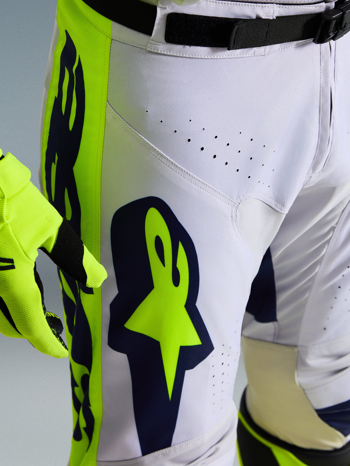 Alpinestars 2026 Racer Air Riway byxor, närbild på vita och marinblå motocrossbyxor med livfulla gula paneler, laserskurna ventilationshål för luftflöde och tydlig Astar-logotyp, kombinerad med matchande gul handske
