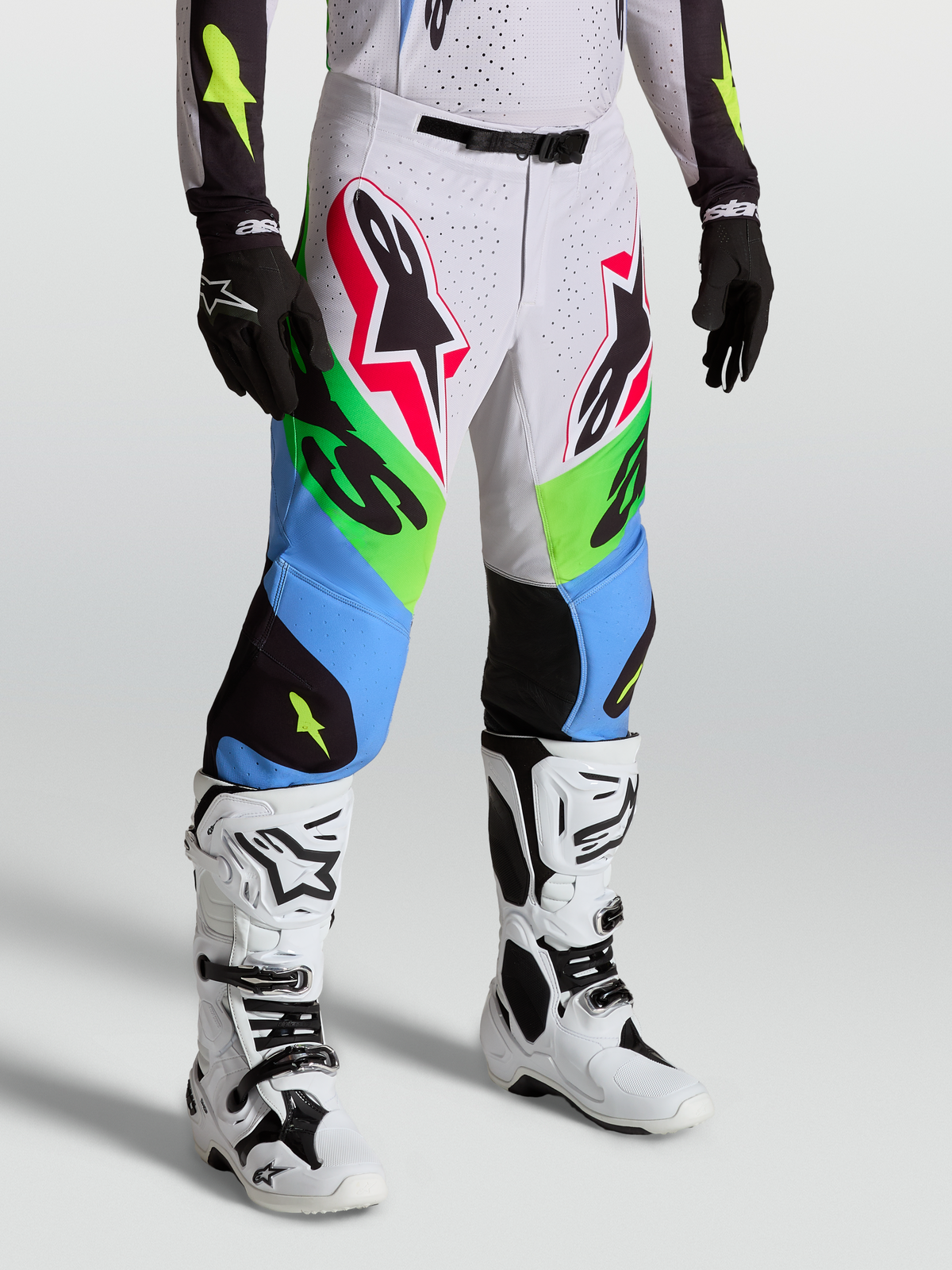 Alpinestars Supertech Dyna byxor, professionella motocrossbyxor i grönt och blått, bärs av modell med vita stövlar och svarta handskar.