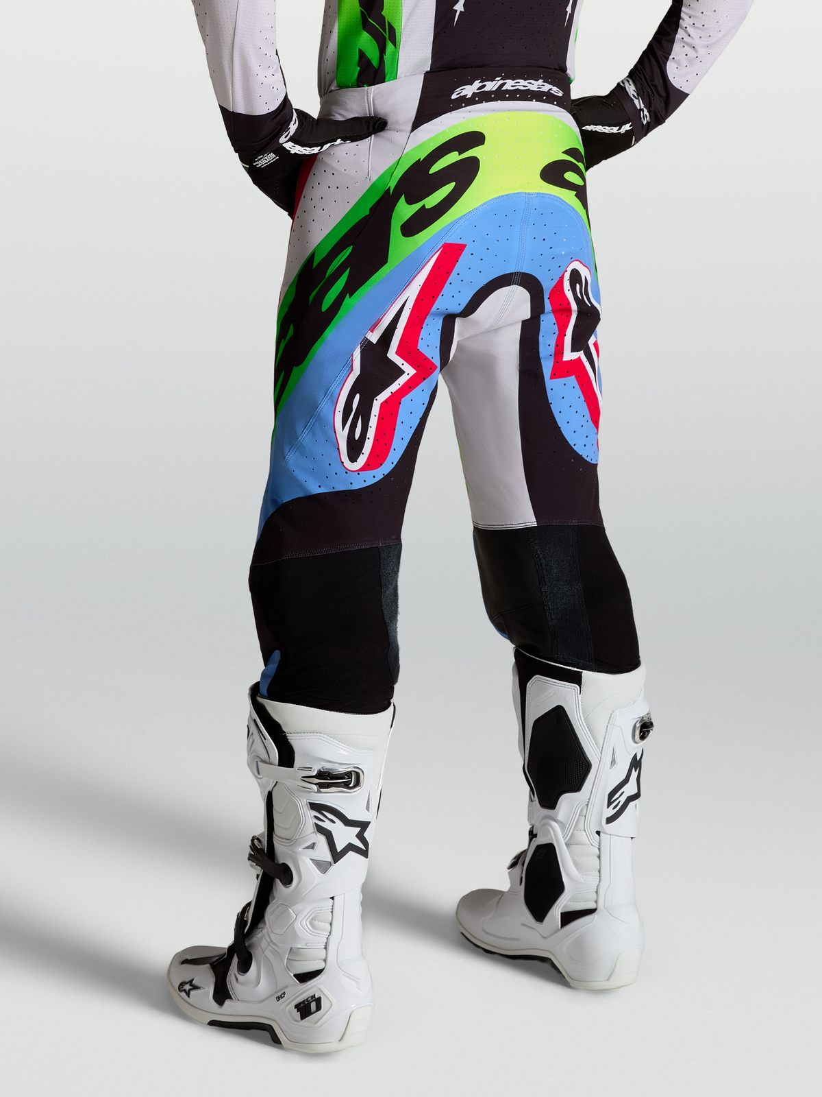 Alpinestars Supertech Dyna Byxor, motocrossbyxor för herr, ljuslila, gröna och svarta med perforeringar och knäpaneler i getläder, bärs av en modell bakifrån med vita Tech 10-stövlar.