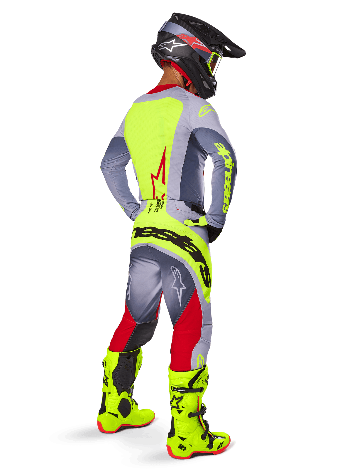 Motocrossförare sedd bakifrån i trekvartsvy, bär Alpinestars 2025 Techstar Melt-byxor i klarrött och grått med en framträdande neongul logotyp över sätet, matchande grå och neongul tröja, neongula stövlar och en svart hjälm med neongula goggles, professionell utrustningsuppsättning för terrängkörning.