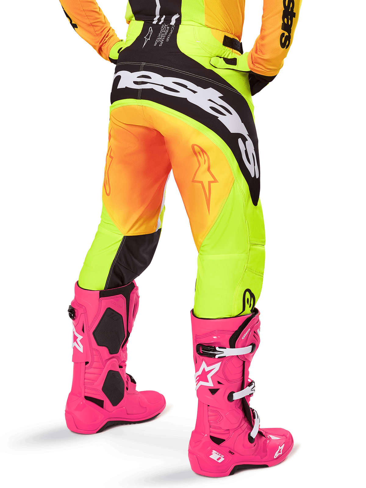 Vy bakifrån av en motocrossförare iklädd Alpinestars 2025 Techstar Melt byxor, gul och orange gradient med svart och vit logotyp på sätet, matchat med neonrosa motocross-stövlar, högpresterande terrängutrustning.