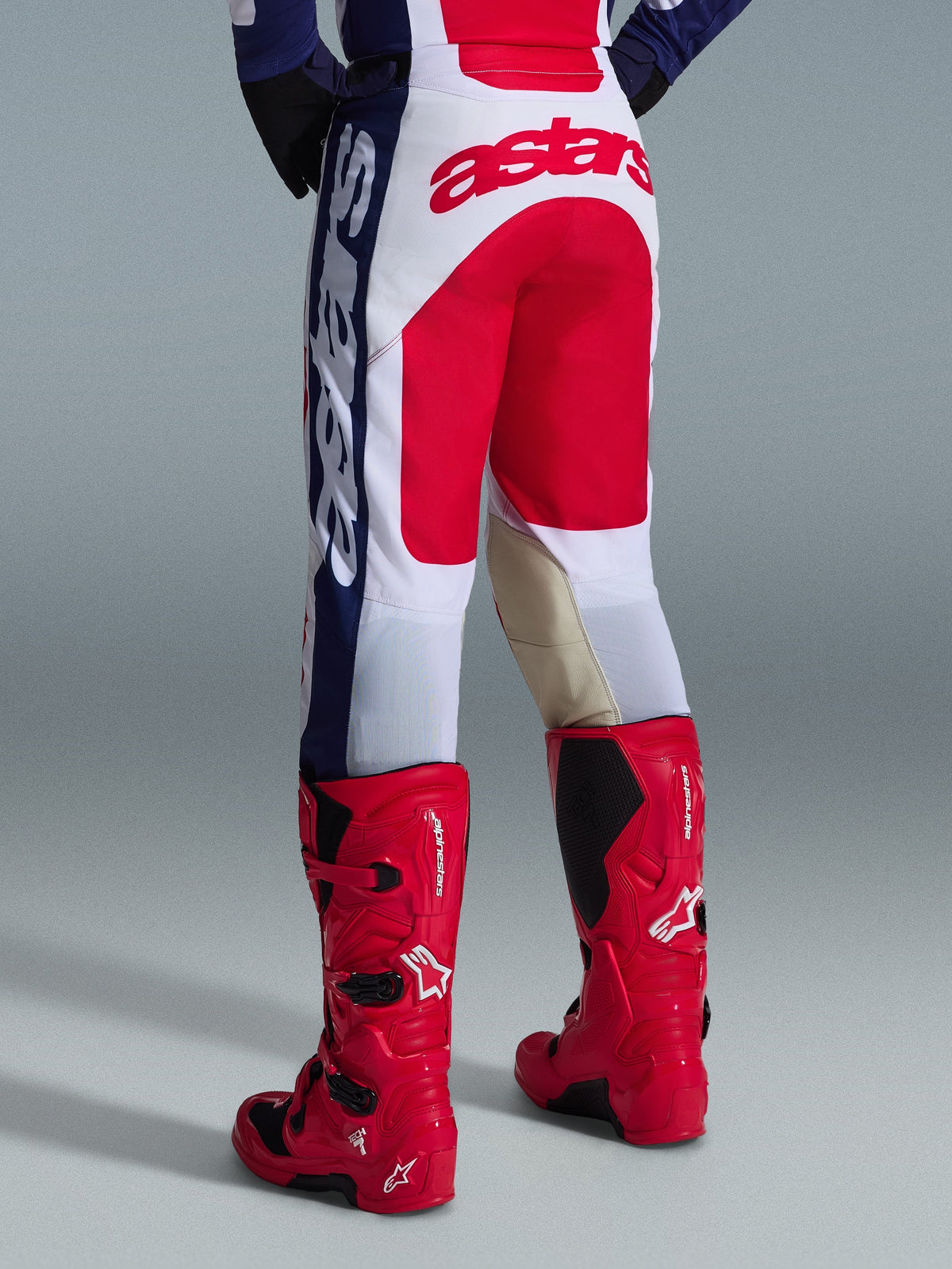 Alpinestars 2026 Racer Riway-byxor, motocrossbyxor, vita, blå och röda, vy bakifrån som visar en stor röd Astars-logotyp på sätet och knäpaneler i beige läder på insidan, bärs med röda Alpinestars motocross-stövlar, prestandautrustning för terrängkörning