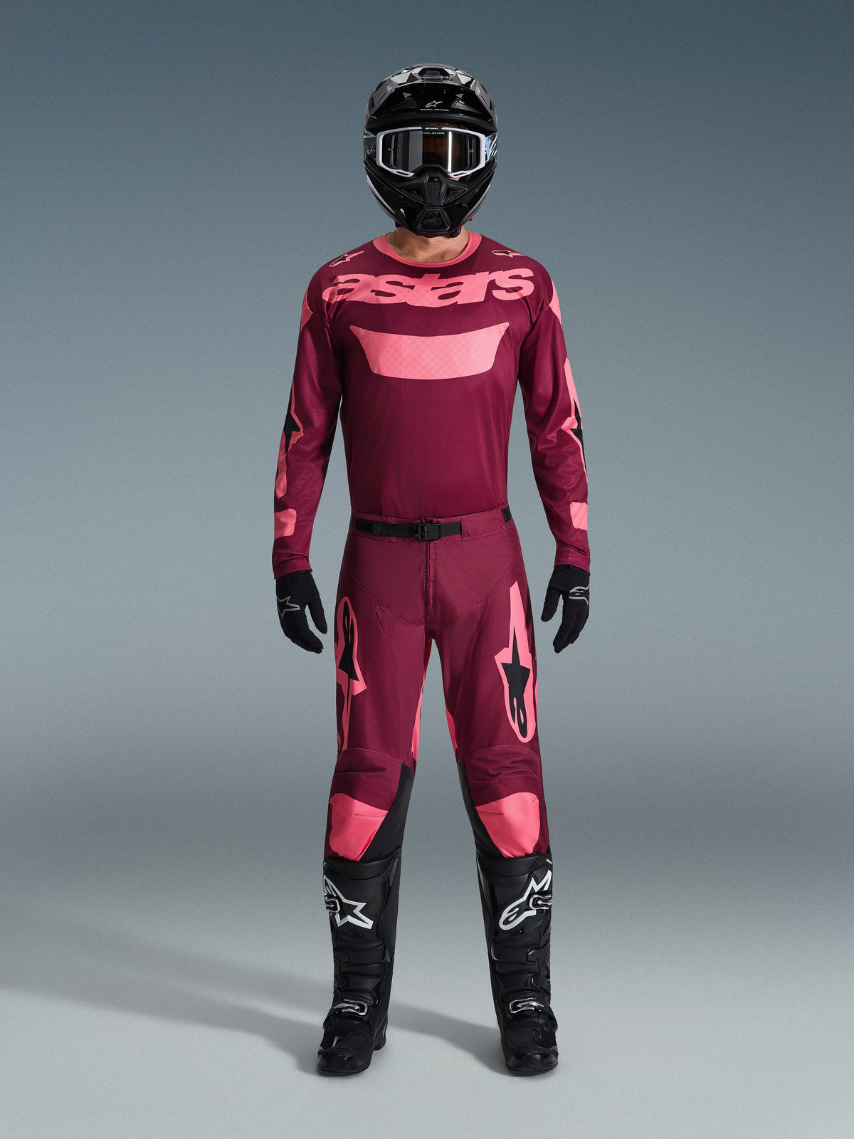 Motocrossförare i komplett racingutrustning, 2026 Racer Riway Jersey i mörkröd och korall, matchande mörkröda byxor med korallfärgade detaljer, svart hjälm med vita detaljer, svarta stövlar med vita logotyper och svarta handskar, koordinerad outfit för terrängkörning