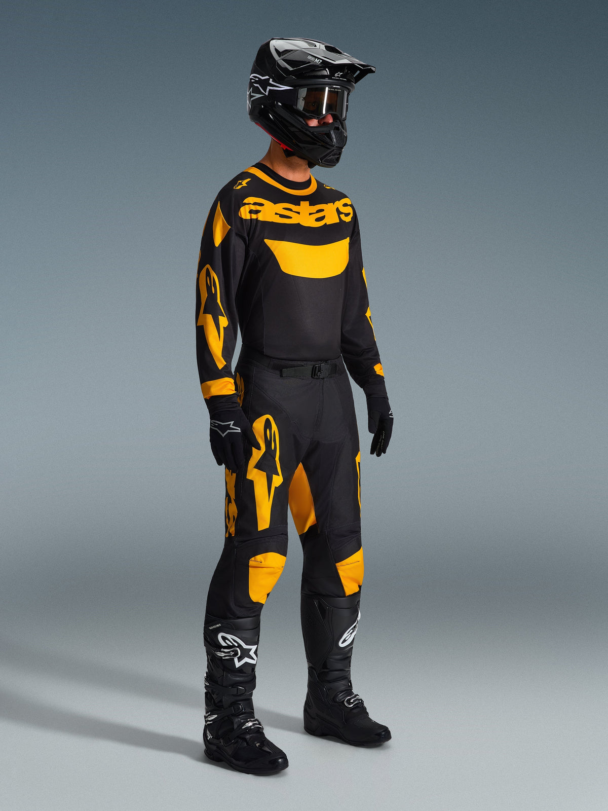 Motocrossförare som bär Alpinestars 2026 Racer Riway-byxor i gult och svart, stylad med en matchande svart och gul 'astars'-tröja, svart hjälm med goggles och svarta racingstövlar, koordinerad utrustning för offroad-prestanda.