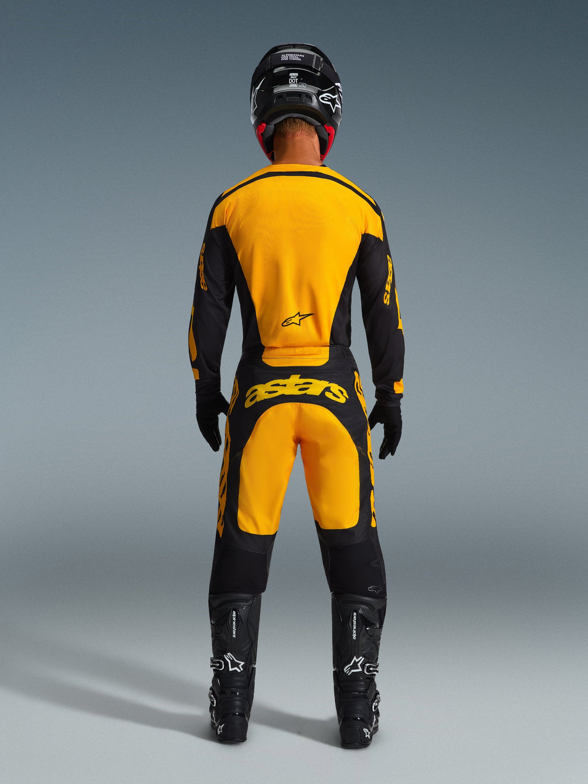 Motocrossförare sedd bakifrån, Alpinestars 2026 Racer Riway-byxor och matchande tröja i gult och svart, framträdande gul branding på ryggen och sätet, svart hjälm, svarta handskar och svarta motocross-stövlar, komplett utrustningsset för terrängkörning