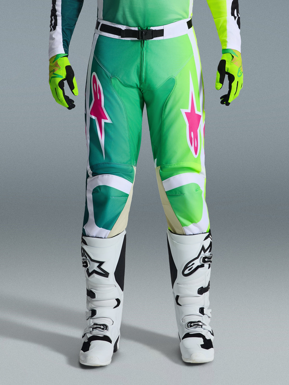Alpinestars 2026 Racer Portl byxor, motocrossbyxor, gröna, vita och svarta med rosa stjärnlogotyper, bärs med vita och svarta stövlar och limegröna handskar, med en gradientdesign och ergonomisk passform för terrängkörning