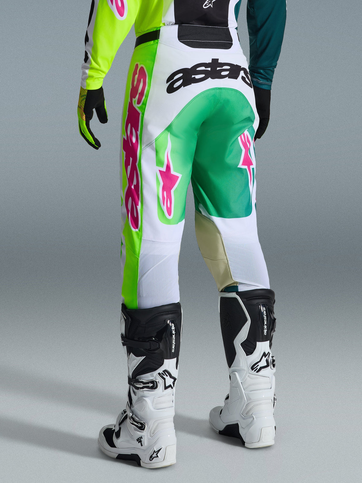 Alpinestars 2026 Racer Portl byxor, motocrossbyxor, gröna, vita och svarta med rosa detaljer, vy bakifrån med framträdande 'astars'-logotyp på sätet och rosa stjärnlogotyper på benen, matchade med vita och svarta motocross-stövlar, prestandautrustning för terrängkörning