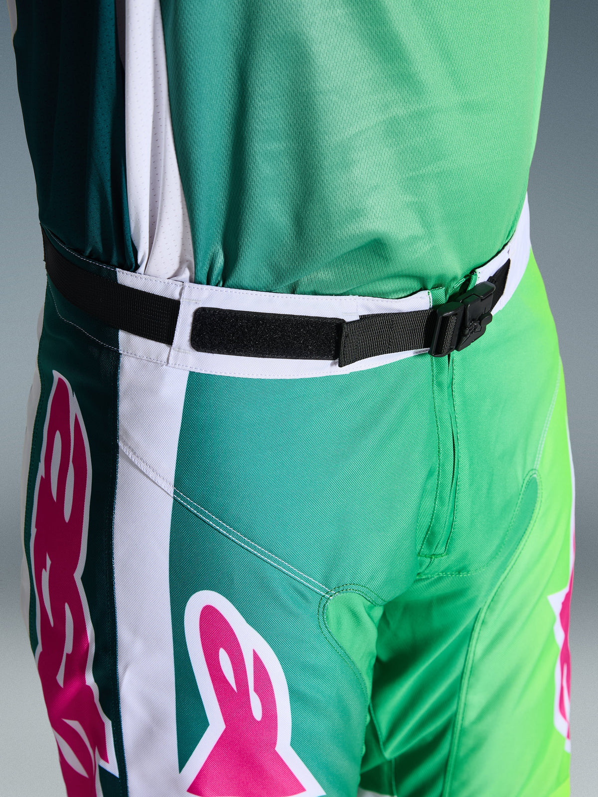 Alpinestars 2026 Racer Portl byxor, motocrossbyxor, gröna, vita och svarta med rosa logotypdetaljer, närbild på midjan som visar det magnetiska SX2-spännet och den justerbara stängningen, hållbar utrustning för terrängkörning