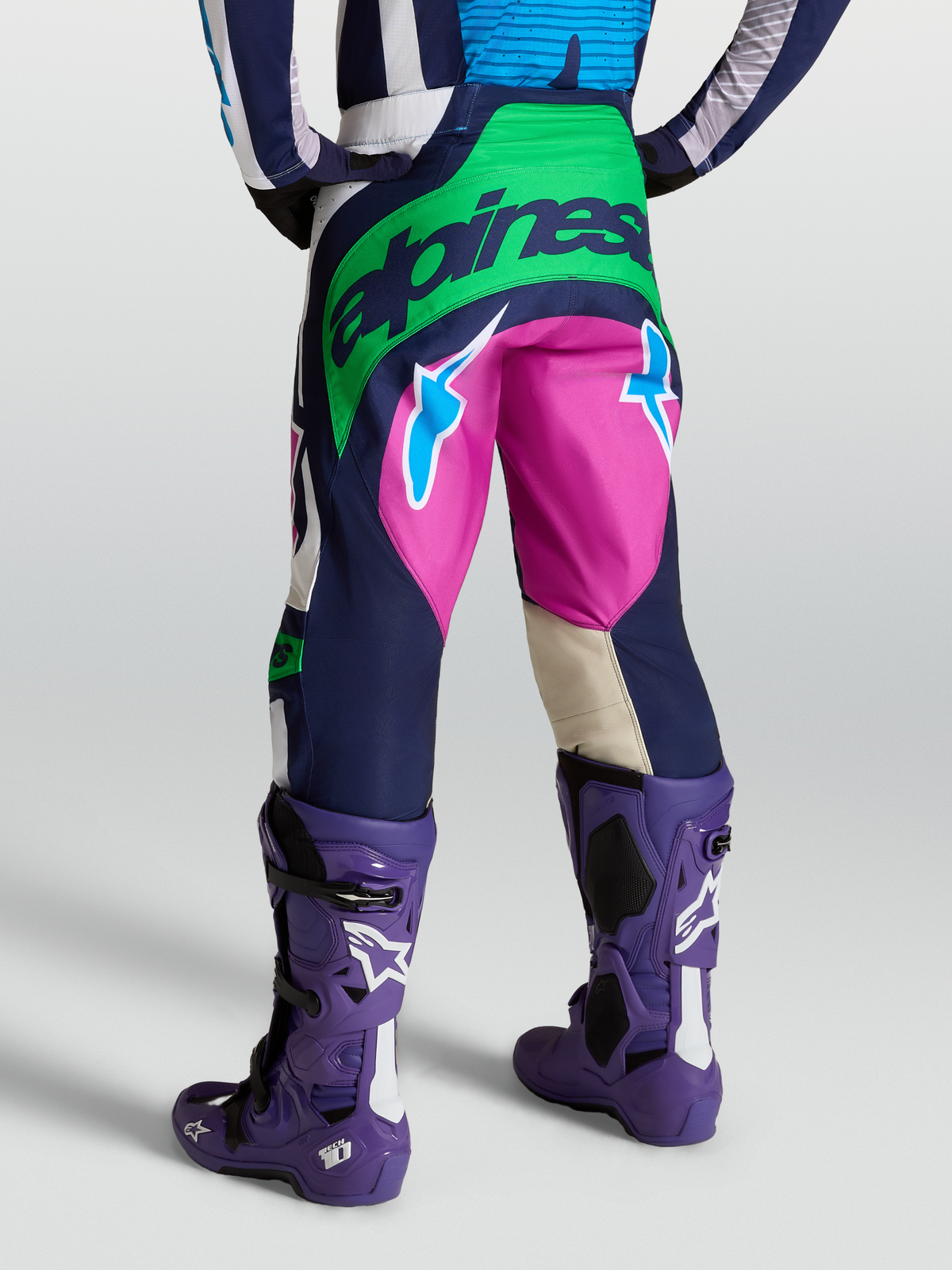 Alpinestars Techstar Maven byxor, motocrossbyxor i blått och grönt, vy bakifrån på modell med lila Tech 10 stövlar.