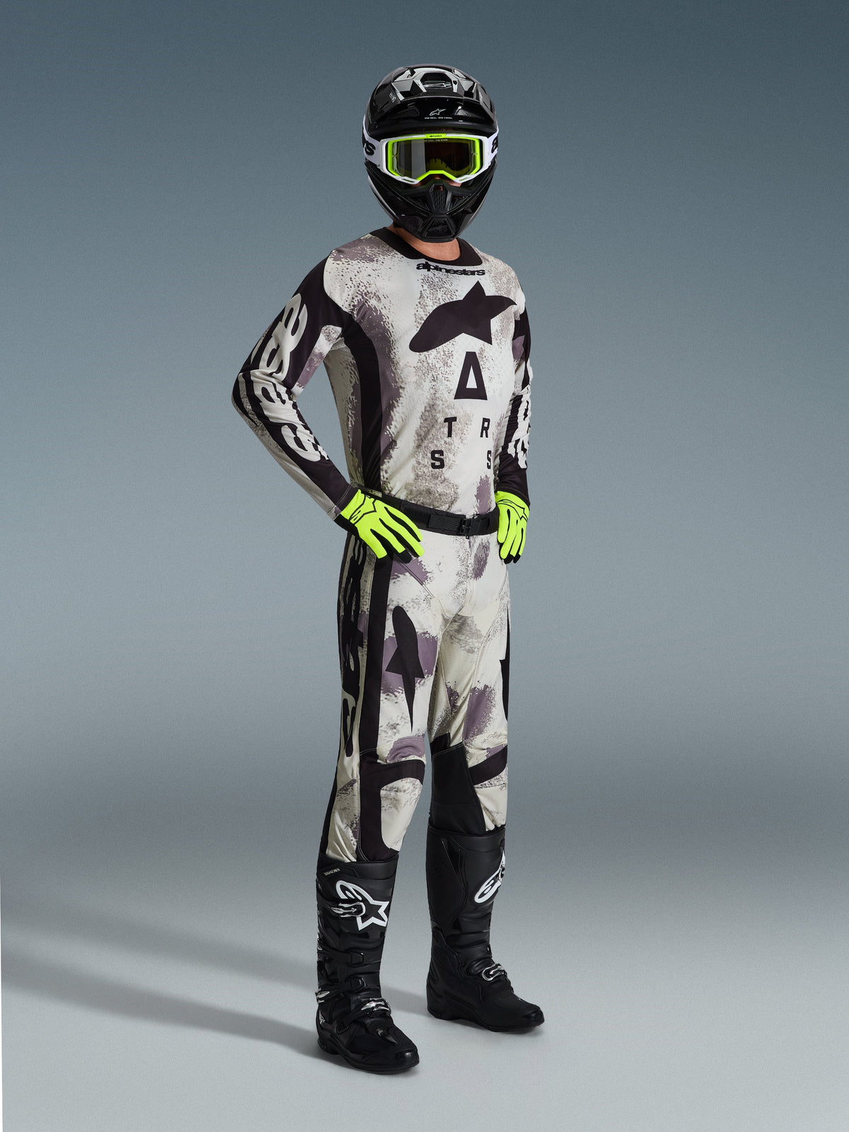 Alpinestars 2026 Racer Lahnd Gear Set, Motocross rider wearing full racing gear in Sand Camo and Gray, matching jersey and pants with black accents and bold branding, neon yellow goggles and gloves, black helmet, and black boots.