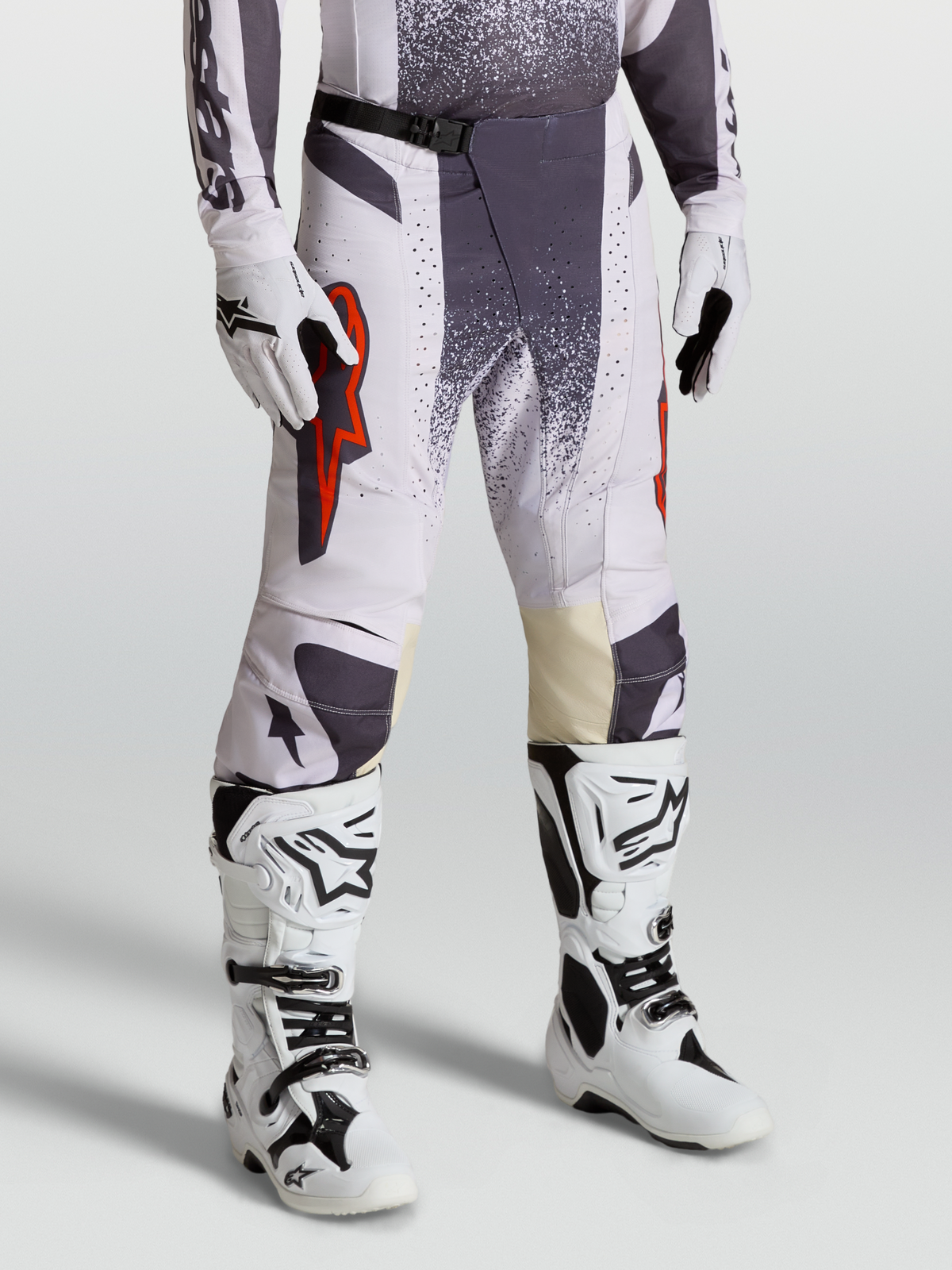 Alpinestars Techstar Swan byxor, motocrossbyxor för herr, ljuslila och mörkgrå med röda fluo-detaljer, modellbild med matchande handskar och vita stövlar för terrängkörning.