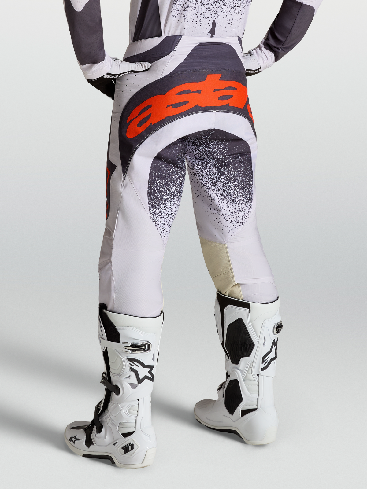 Alpinestars Techstar Swan byxor, motocrossbyxor för herrar, ljuslila och mörkgrå med röd fluo-logotyp, med vita Tech 10 stövlar.