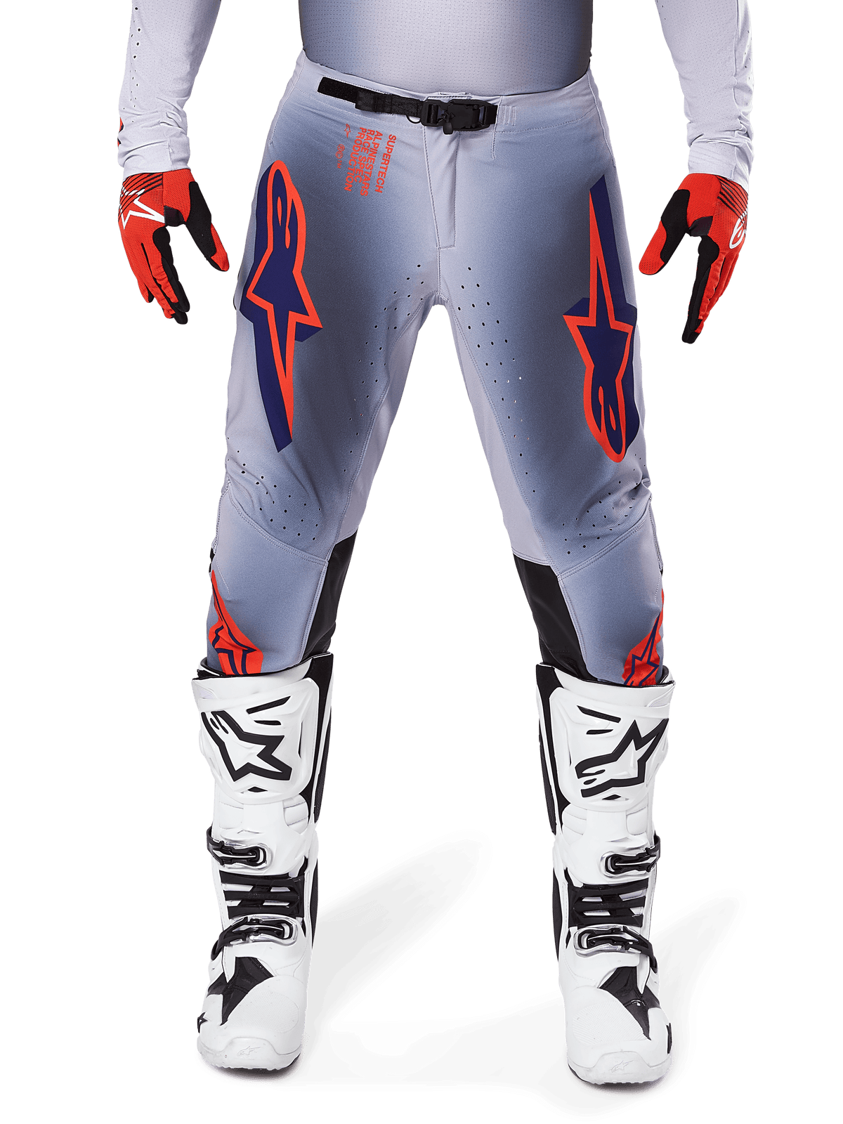 Alpinestars 2025 Supertech Lipan byxor, motocrossbyxor, grå och orange fluo, bärs med röda och svarta handskar och vita och svarta stövlar, med stora Alpinestars-stjärnlogotyper på låren och ventilationsperforeringar för racing på proffsnivå.