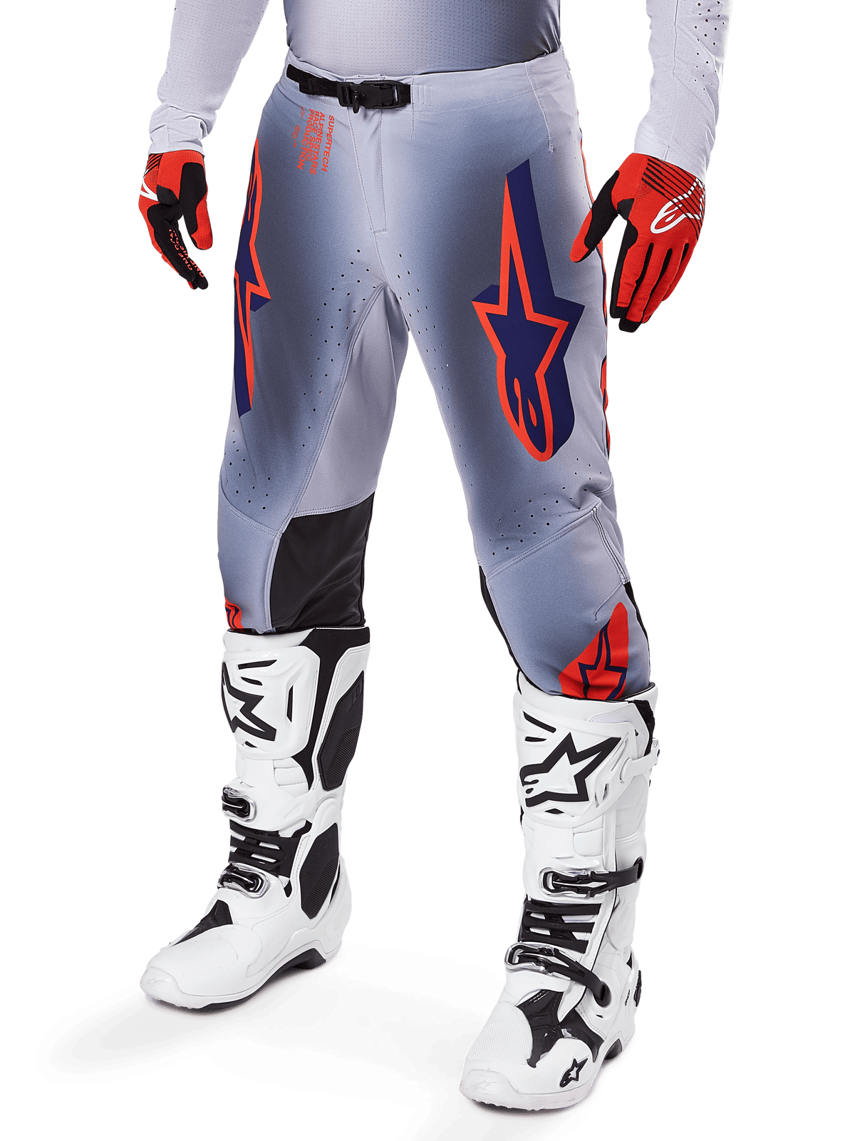 Alpinestars 2025 Supertech Lipan-byxor, motocrossbyxor, grå och orange fluo, med marinblå stjärndesign och svarta paneler på innerknäna, bärs med röd-orangea handskar och vita stövlar, professionell racingutrustning för terrängkörning