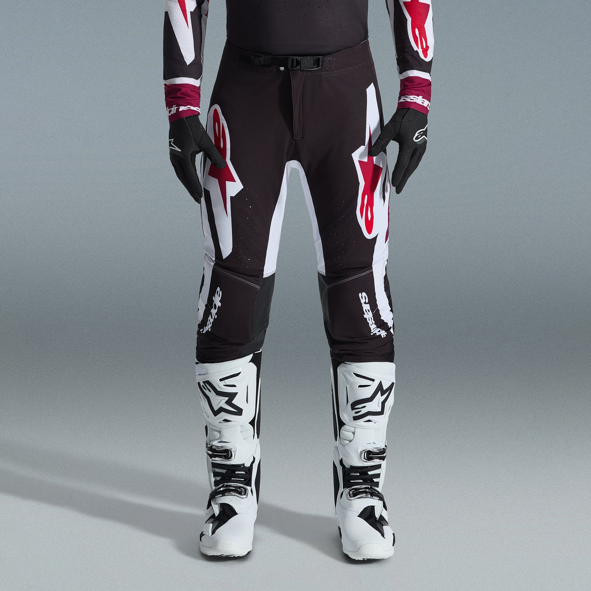 Alpinestars 2026 Supertech AFD Vista utrustningsset, motocrossförare klädd i svarta byxor med stora vita och röda logotyper, matchande funktionströja med vinröda muddar, svarta handskar och vita professionella racingstövlar, högpresterande outfit för terrängracing