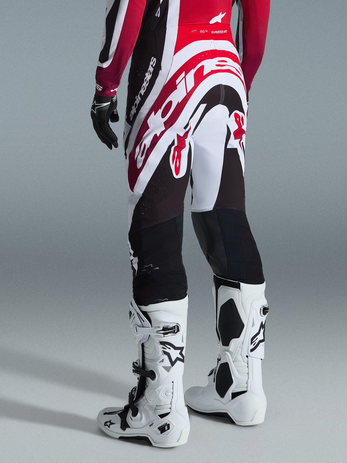 Alpinestars 2026 Supertech AFD Vista-byxor, motocrossbyxor, svarta, röda och vita, vy bakifrån på en förare, bärs tillsammans med vita Tech 10-stövlar och matchande tröja, atletisk tävlingspassform för elitprestanda i terräng