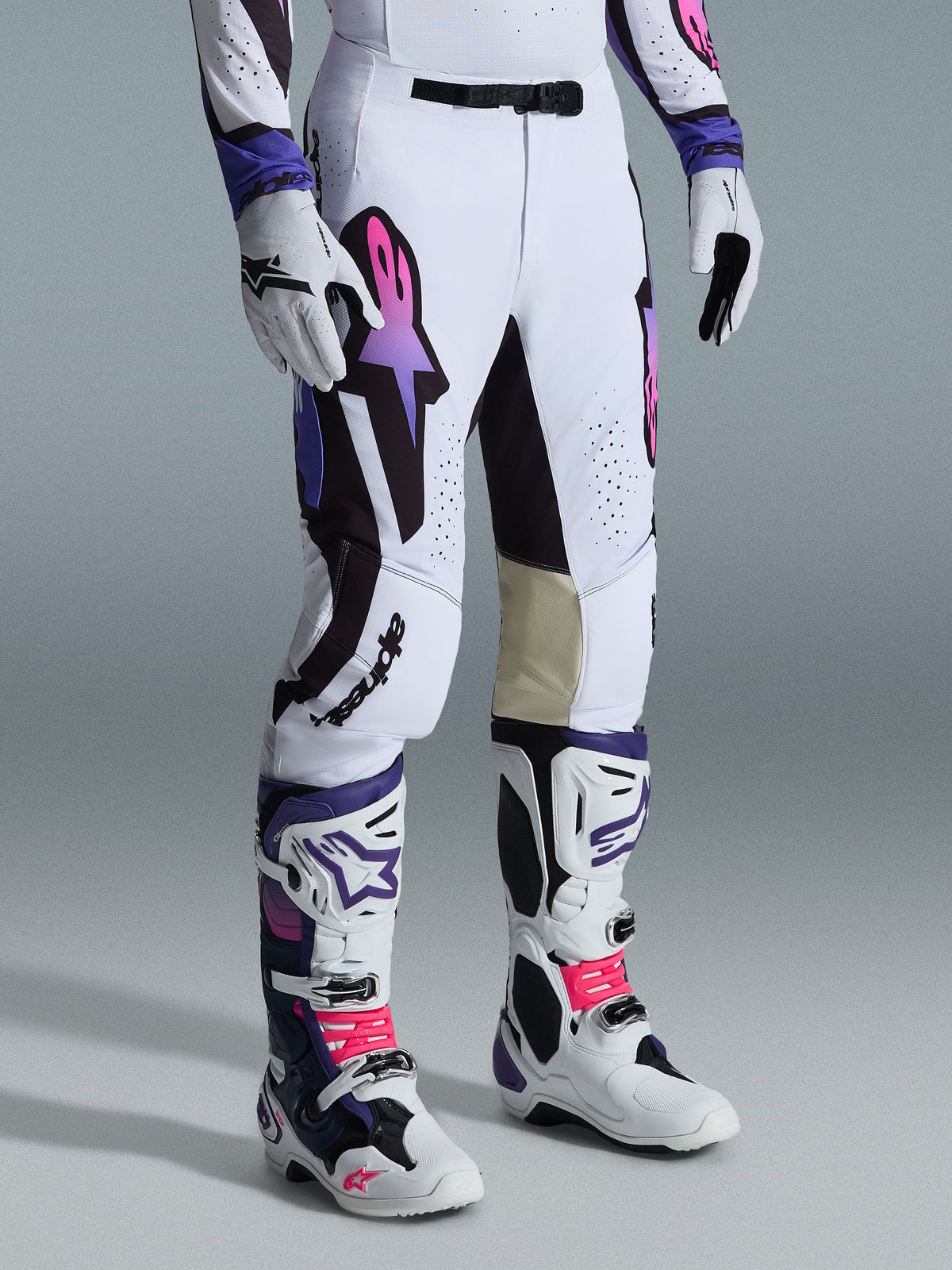 Alpinestars 2026 Supertech AFD Vista Pants, Motocross Pants, White Purple and Black, featuring a gradient pink and purple Astar logo, worn with matching white and purple motocross boots and gloves, athletic race fit with tan leather inner knee panels and perforated detailing.