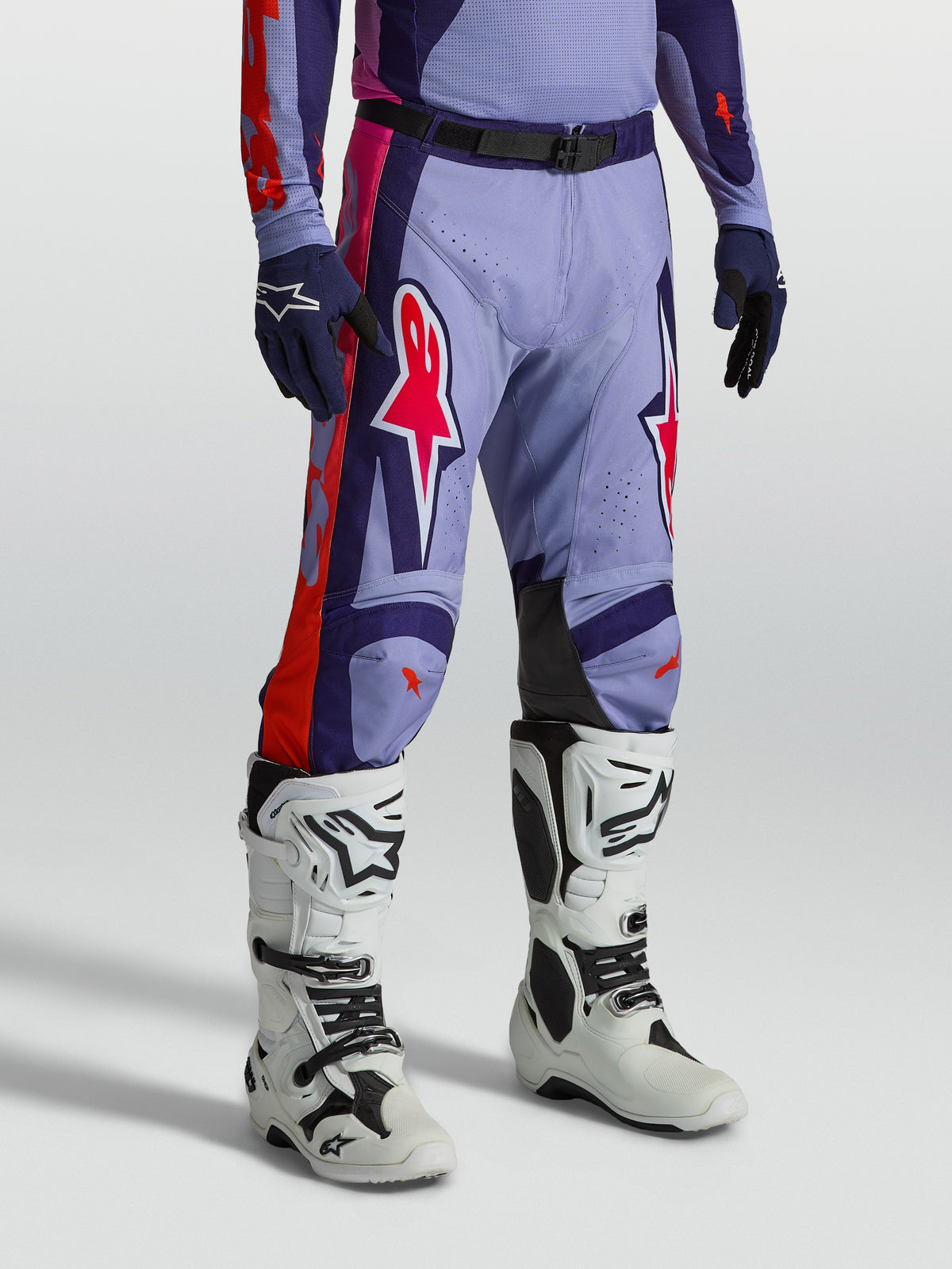 Alpinestars Racer Air Hunt byxor, ventilerade lila och rosa motocrossbyxor för herrar, visas på modell med vita motorcykelstövlar, tekniskt material för terrängkörning