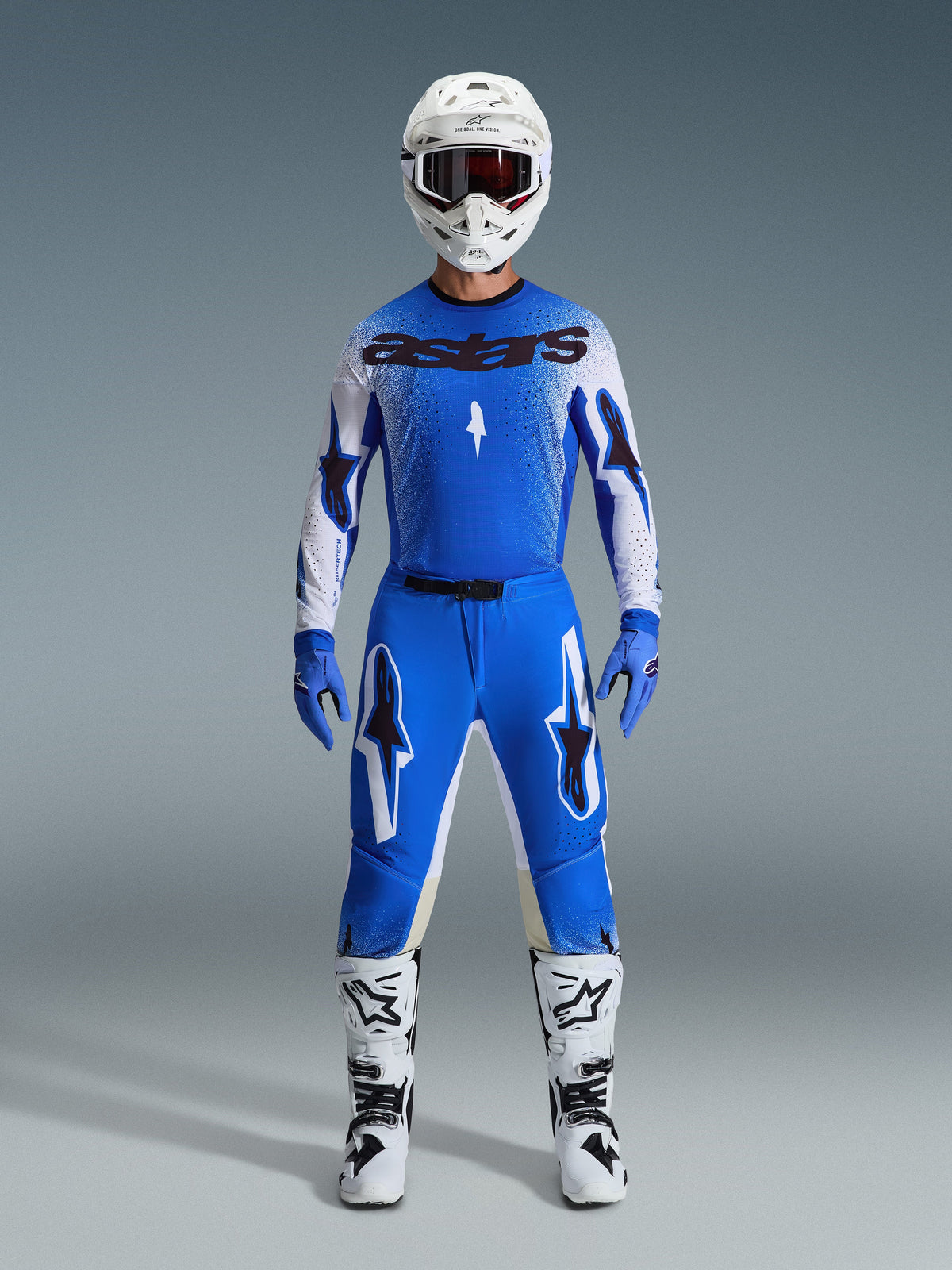Motocrossförare i komplett racingutrustning, blå och vit tröja med svart astars-branding, 2026 Supertech Scenz-byxor i Ucla Blue White med stora stjärnlogotyper, vit hjälm, blå handskar och vita stövlar, matchande atletisk racingoutfit
